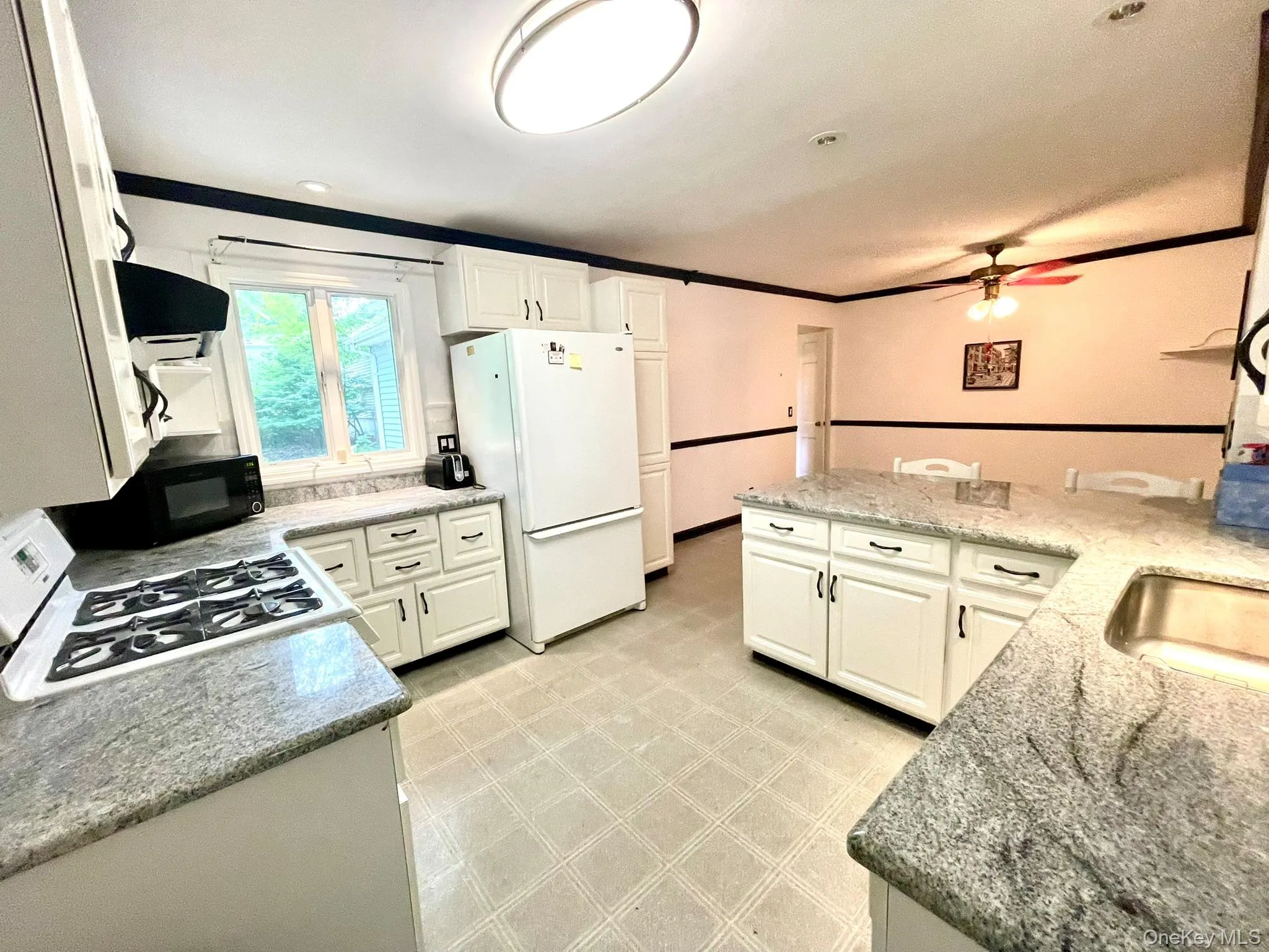 Kitchen featuring extensive white cabinetry, speckled countertops, a gas range, and a ceiling fan Kitchen featuring extensive white cabinetry, speckled countertops, a gas range, and a ceiling fan