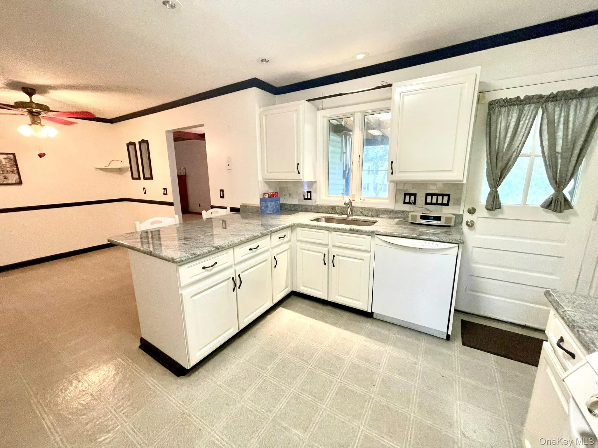 Open-concept kitchen featuring white cabinetry, light-toned granite-style countertops, and a built-in dishwasher Open-concept kitchen featuring white cabinetry, light-toned granite-style countertops, and a built-in dishwasher