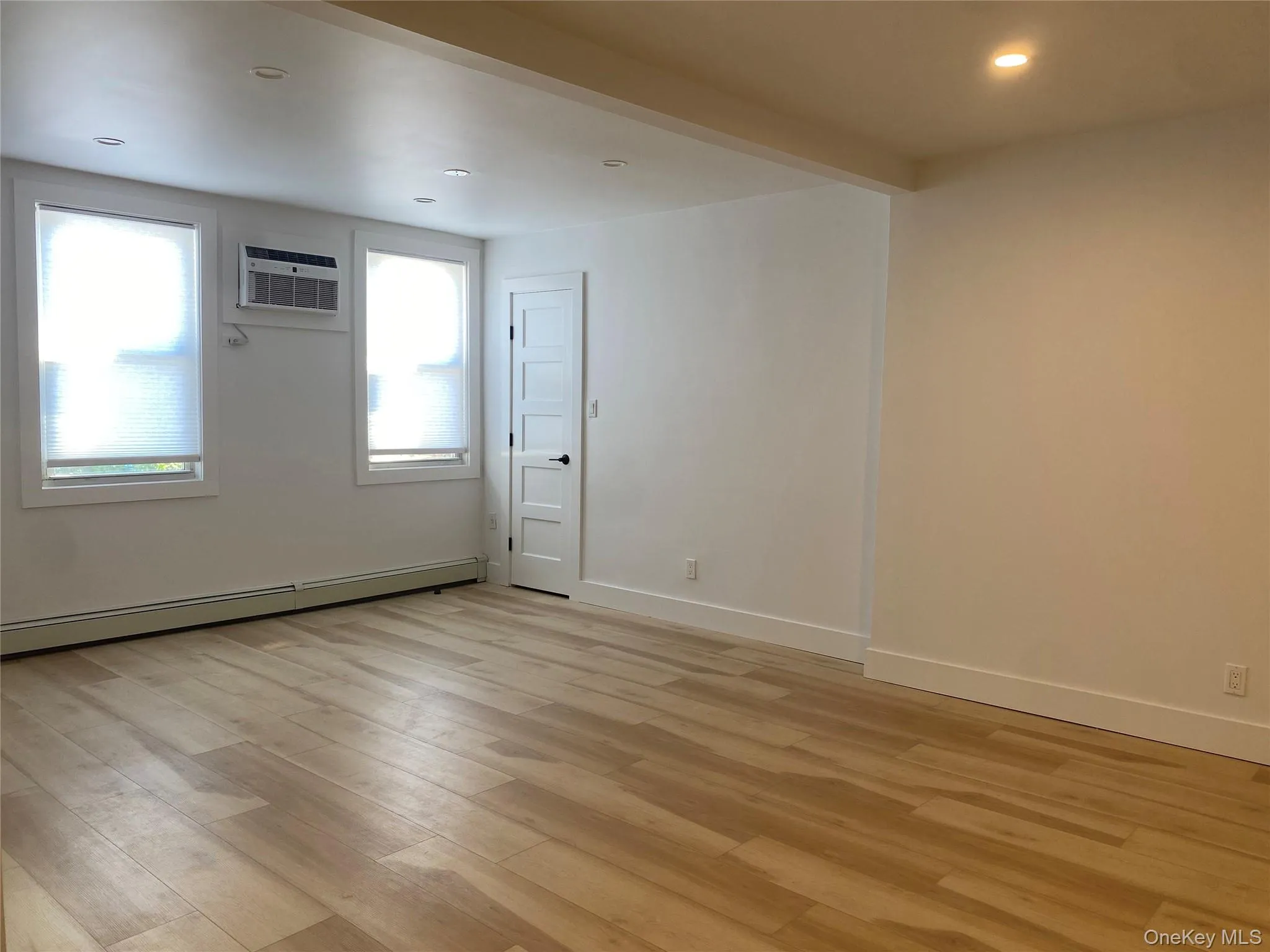Living room featuring light wood-style flooring, a baseboard heating unit, recessed lighting, beamed ceiling, and a wall mounted AC Living room featuring light wood-style flooring, a baseboard heating unit, recessed lighting, beamed ceiling, and a wall mounted AC