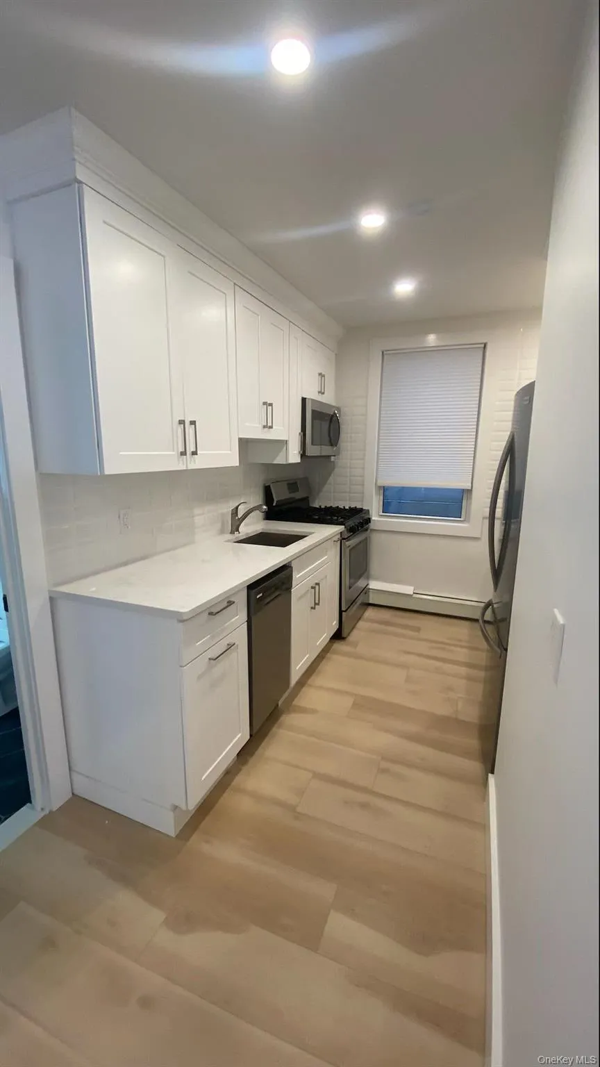Kitchen with tile backsplash, white cabinetry, stainless steel appliances, light wood-style flooring, and light stone countertops Kitchen with tile backsplash, white cabinetry, stainless steel appliances, light wood-style flooring, and light stone countertops