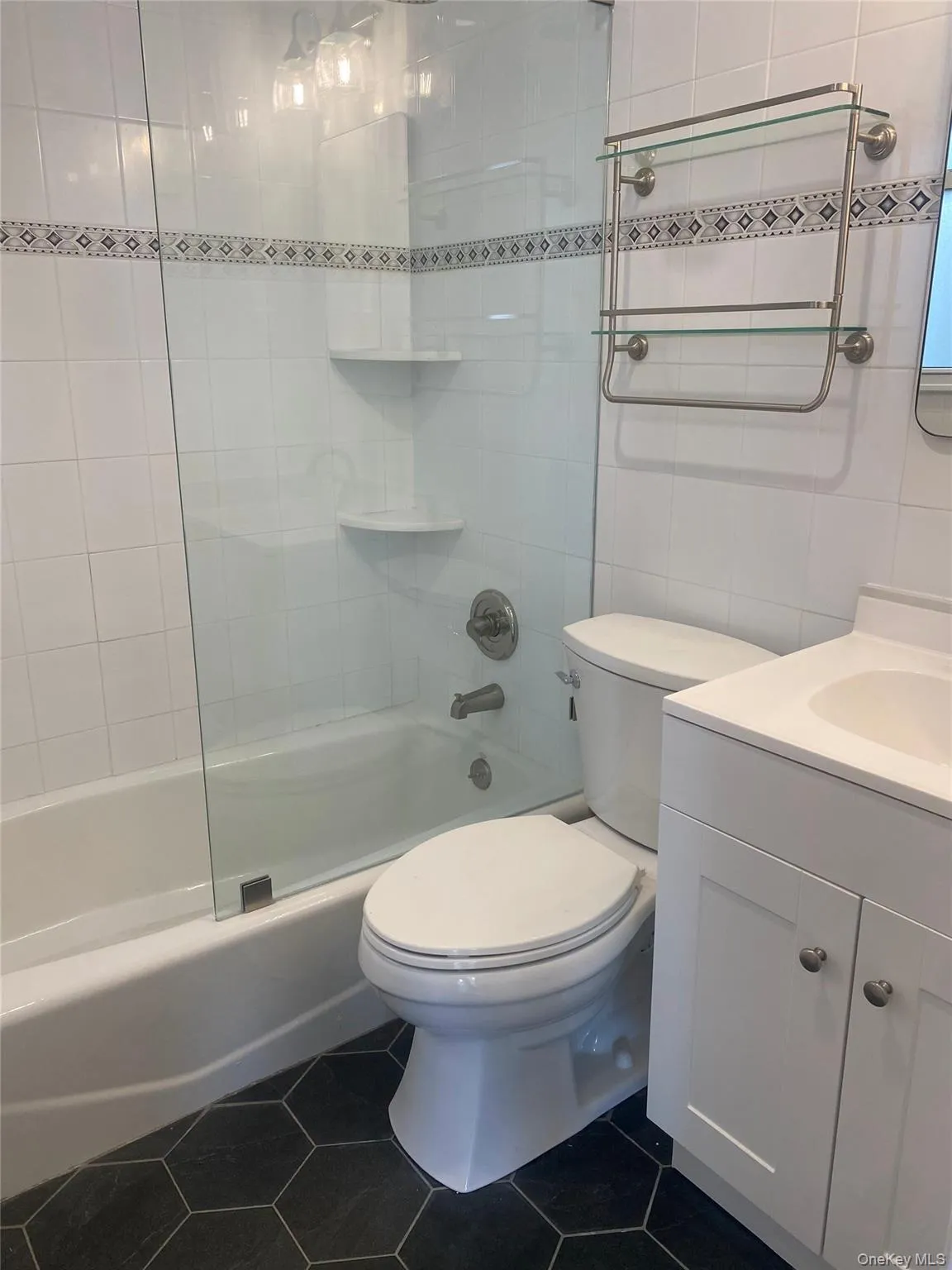 Full bath featuring shower / bathtub combination, vanity, tile walls, and dark tile patterned floors Full bath featuring shower / bathtub combination, vanity, tile walls, and dark tile patterned floors