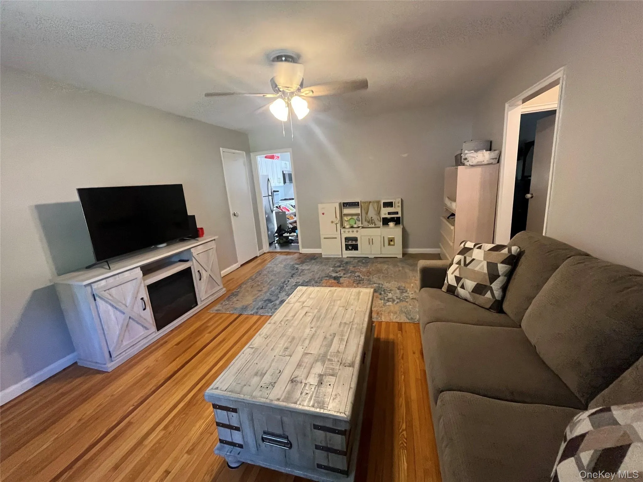 Hardwood flooring throughout a spacious living area featuring a ceiling fan, light gray wall tones, and white trim Hardwood flooring throughout a spacious living area featuring a ceiling fan, light gray wall tones, and white trim
