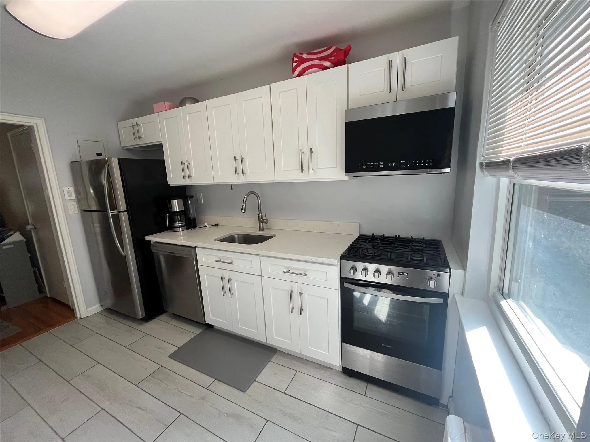 Kitchen featuring white shaker-style cabinetry, light-toned countertops, and stainless steel appliances including a refrigerator, dishwasher, and gas range Kitchen featuring white shaker-style cabinetry, light-toned countertops, and stainless steel appliances including a refrigerator, dishwasher, and gas range
