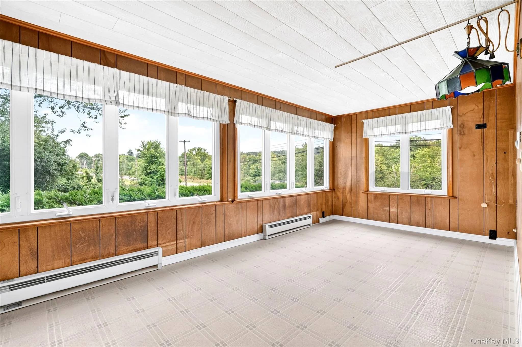 Heated Sunroom with wood-paneled walls with multiple windows, patterned flooring, and a paneled ceiling Heated Sunroom with wood-paneled walls with multiple windows, patterned flooring, and a paneled ceiling