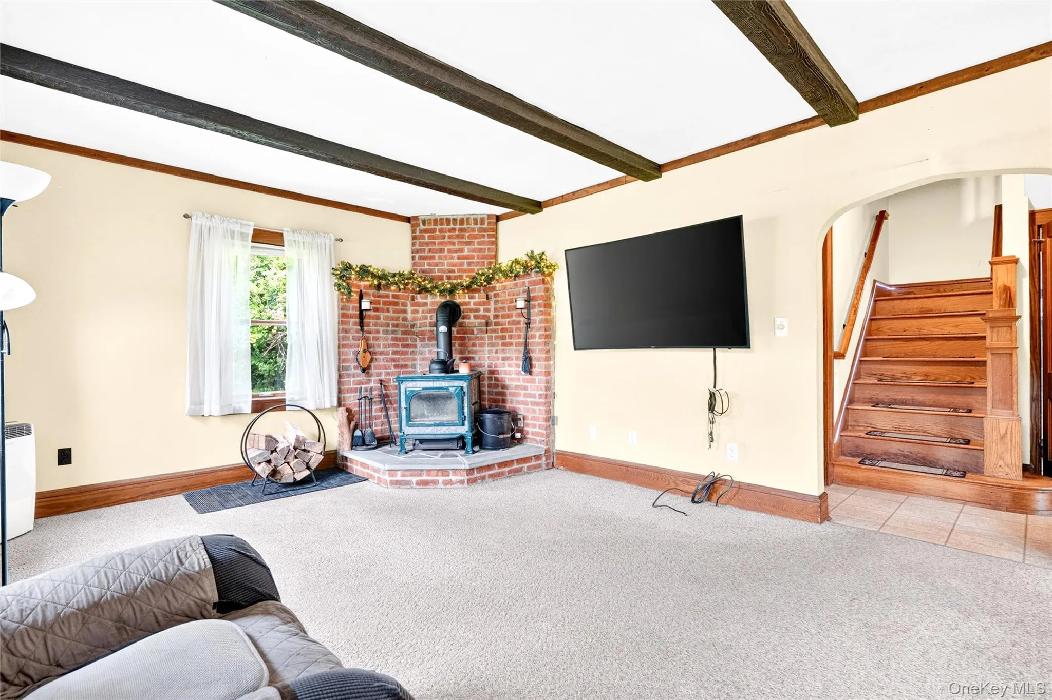 Exposed ceiling beams, brick fireplace with wood-burning stove, natural wood staircase, and light-toned wall finishes Exposed ceiling beams, brick fireplace with wood-burning stove, natural wood staircase, and light-toned wall finishes