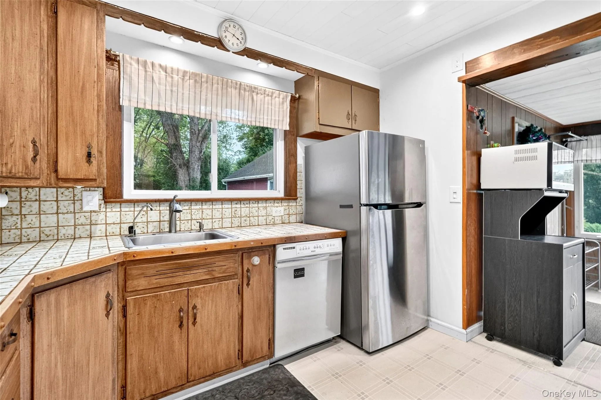 Kitchen featuring wood cabinetry, tiled countertops, stainless steel appliances, and a window above the sink Kitchen featuring wood cabinetry, tiled countertops, stainless steel appliances, and a window above the sink