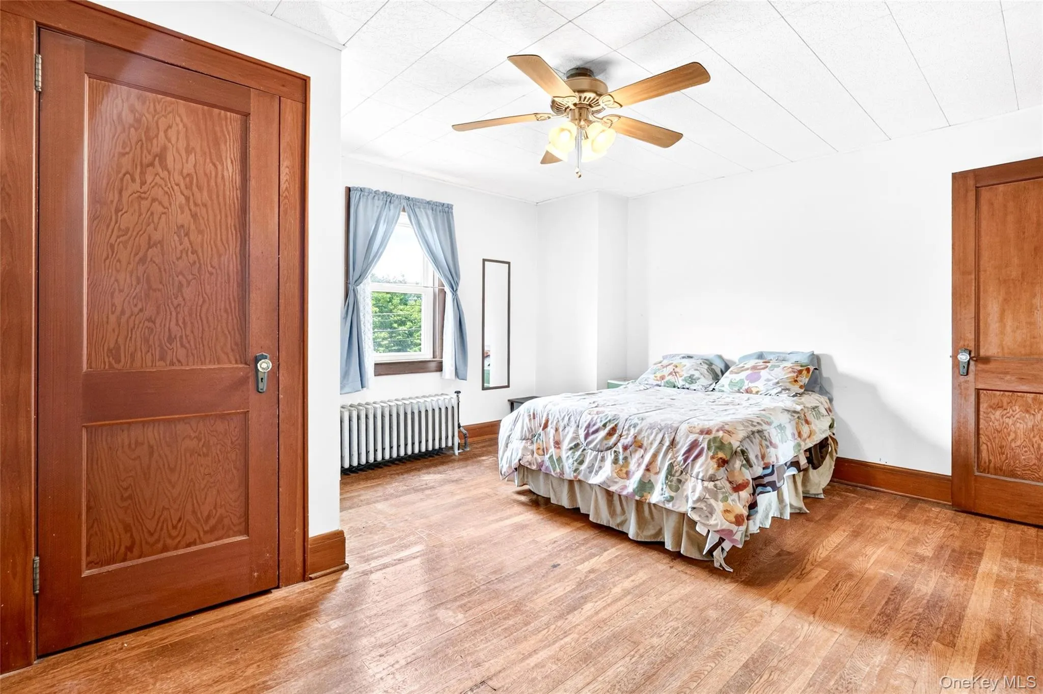 Wood-finish flooring, ceiling fan with integrated lighting, wood panel doors, and window with radiator Wood-finish flooring, ceiling fan with integrated lighting, wood panel doors, and window with radiator