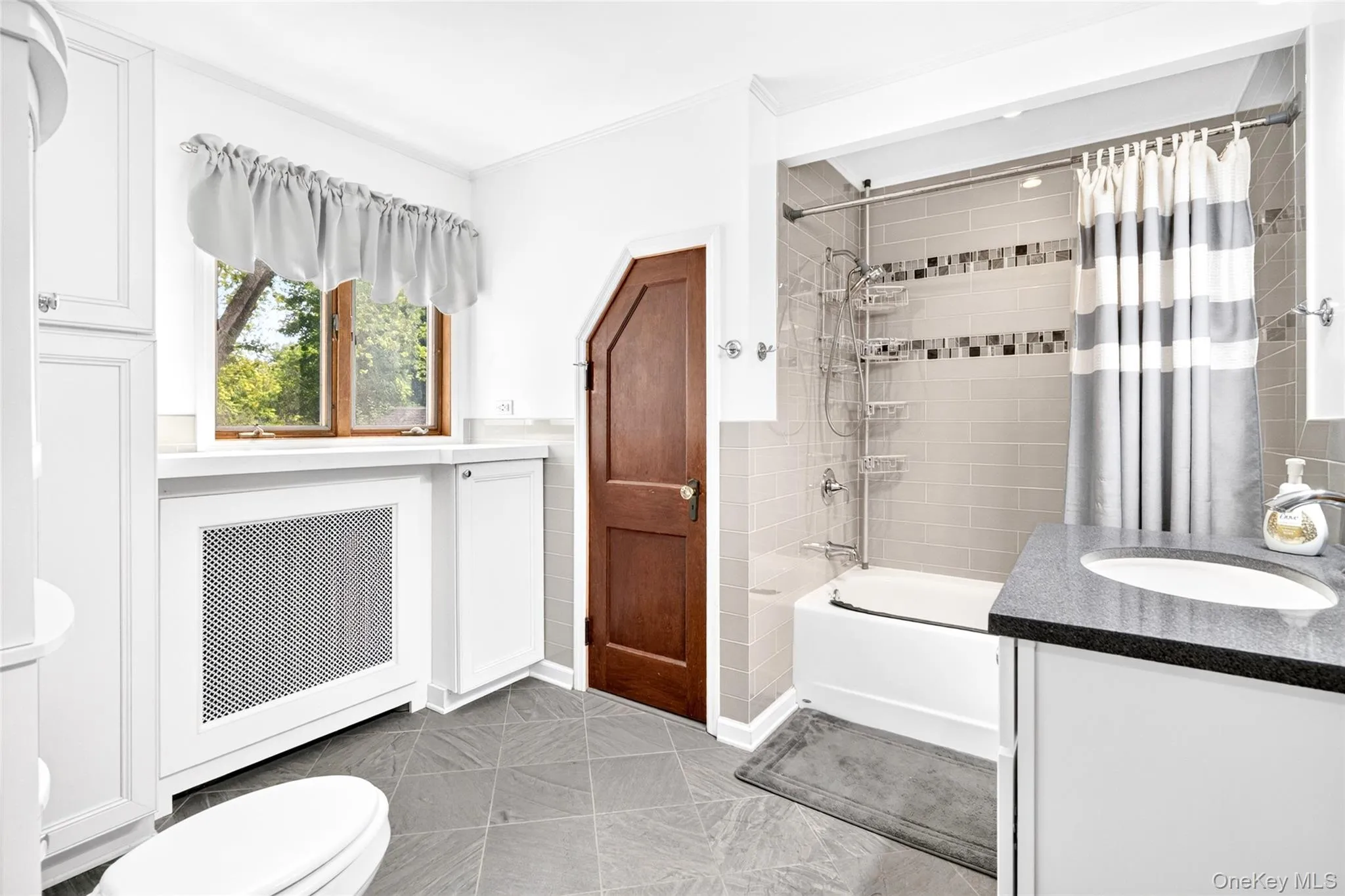 Bathroom featuring a built-in tub with tile surround, a vanity with a dark countertop and undermount sink, and durable tile flooring Bathroom featuring a built-in tub with tile surround, a vanity with a dark countertop and undermount sink, and durable tile flooring