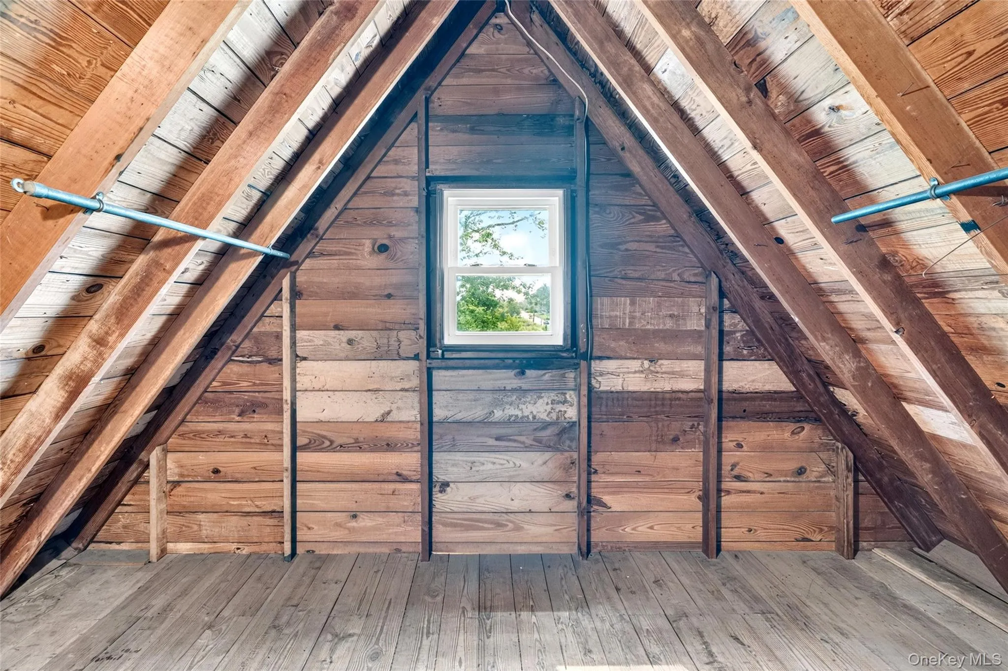 Attic space featuring exposed wood beams, wood paneling, wood flooring, and a single window Attic space featuring exposed wood beams, wood paneling, wood flooring, and a single window