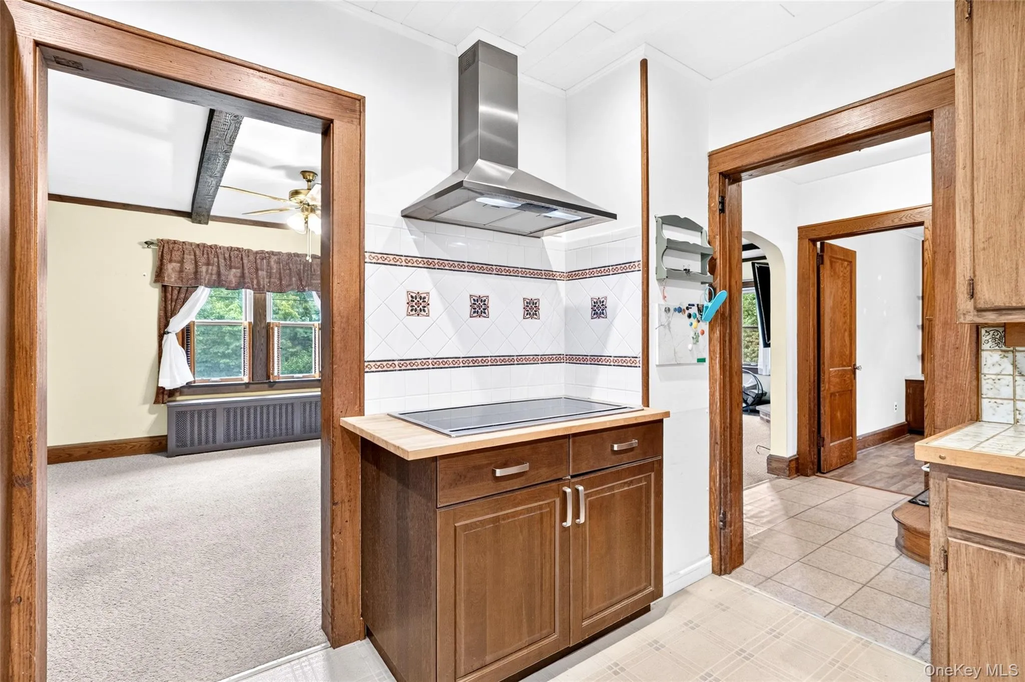 Built-in cooktop with stainless steel range hood, wood-finish cabinetry, and decorative tile backsplash Built-in cooktop with stainless steel range hood, wood-finish cabinetry, and decorative tile backsplash