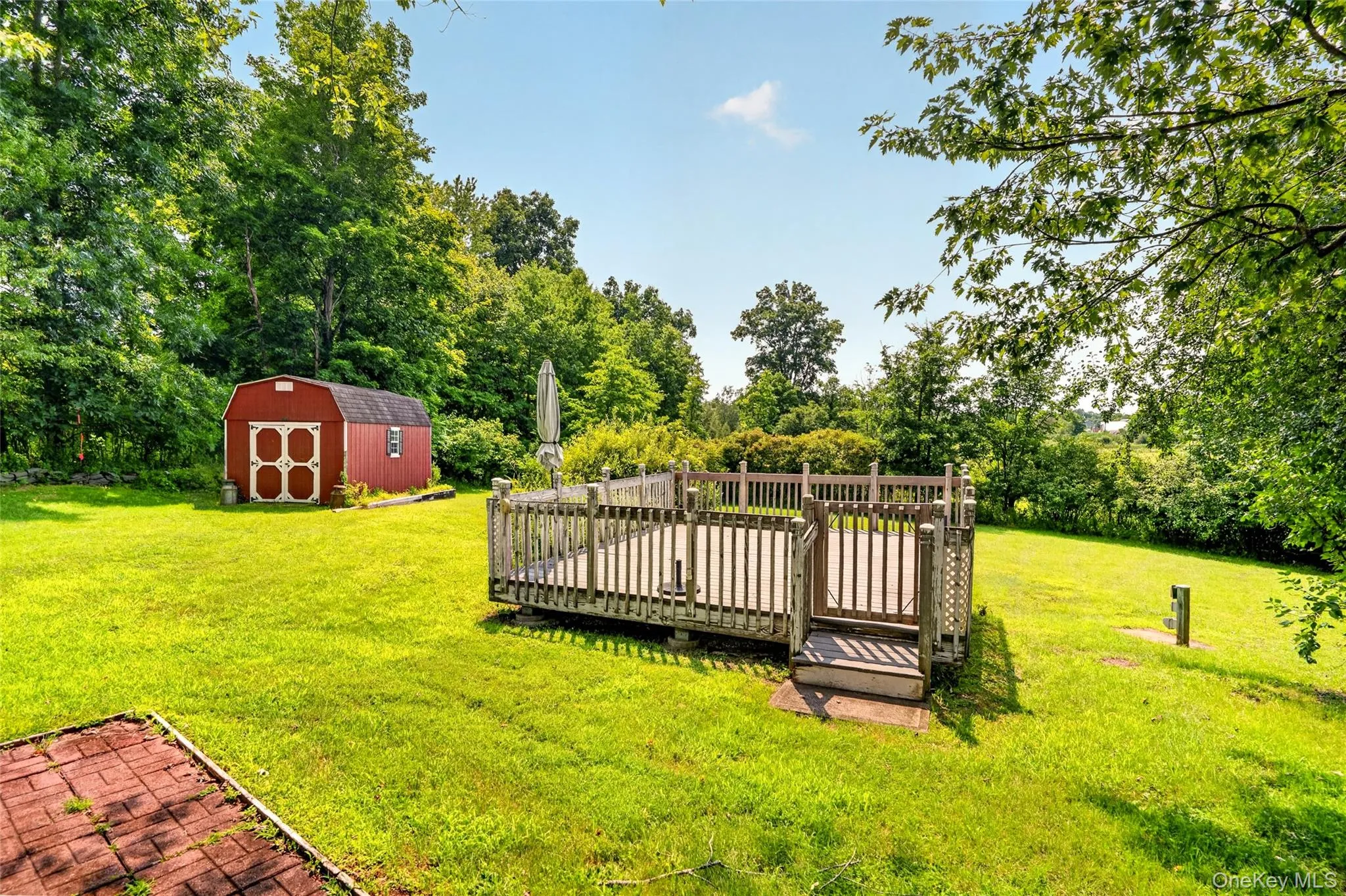 Expansive lawn featuring a raised wood deck, wood railing, and a red storage shed with white trim Expansive lawn featuring a raised wood deck, wood railing, and a red storage shed with white trim