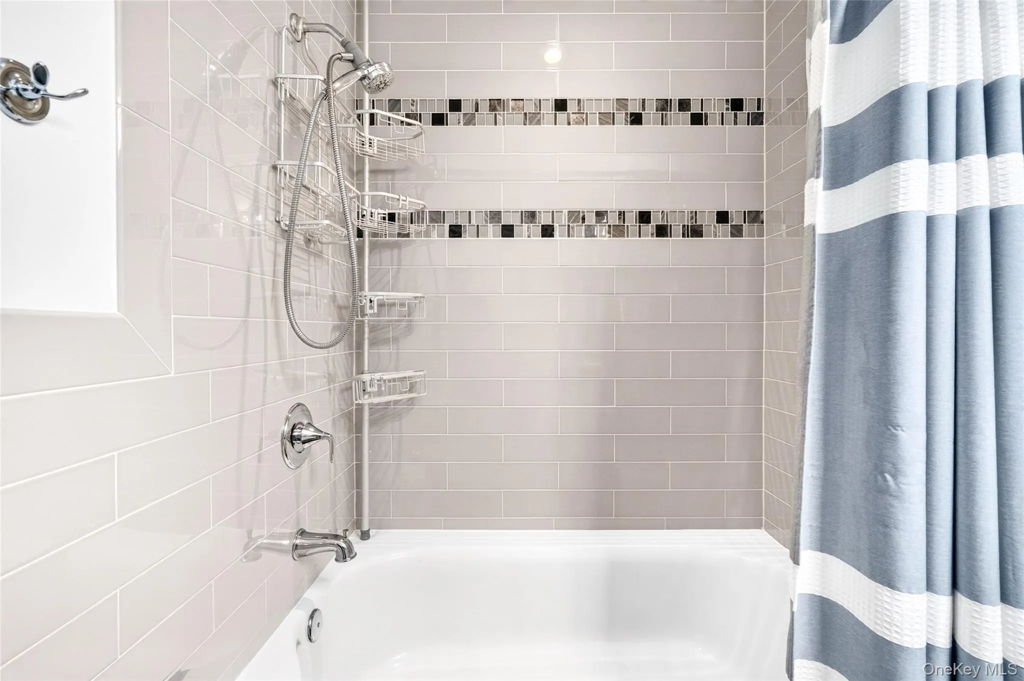 Bathtub with subway tile surround, decorative mosaic tile accents, and chrome fixtures Bathtub with subway tile surround, decorative mosaic tile accents, and chrome fixtures