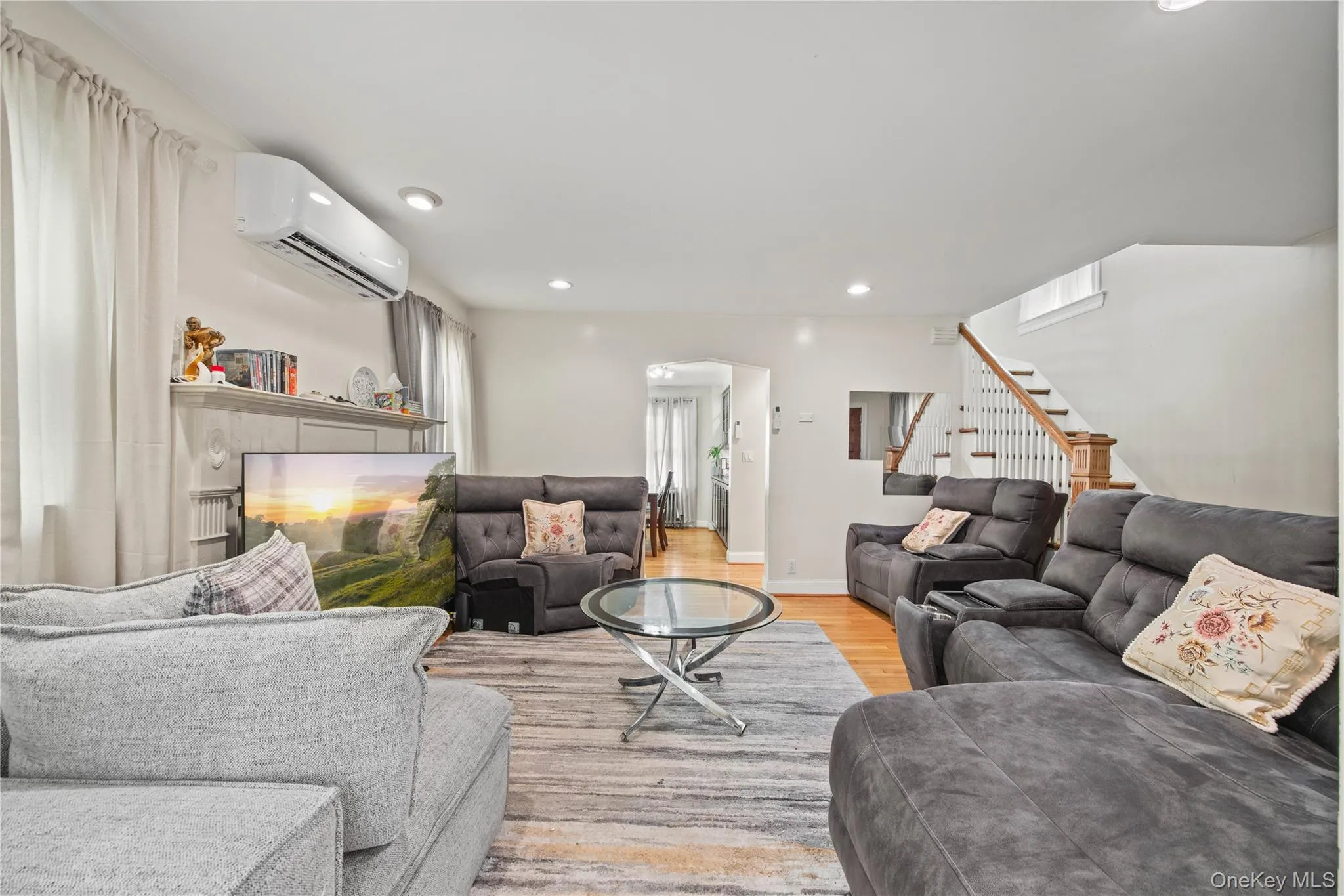 Spacious living area featuring hardwood flooring, recessed lighting, white walls, and a staircase with white balusters and a wood handrail Spacious living area featuring hardwood flooring, recessed lighting, white walls, and a staircase with white balusters and a wood handrail