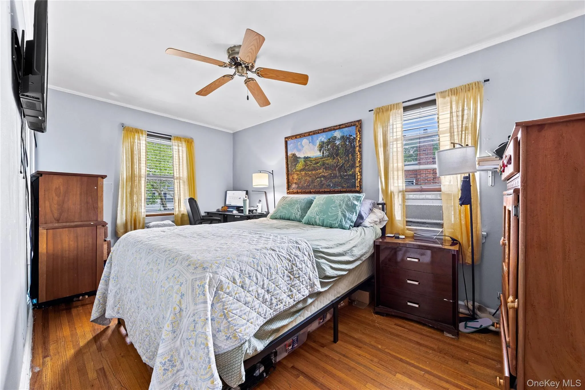 Bedroom 3 - featuring wood-finish flooring, light blue walls, a ceiling fan with integrated lighting, and two windows with blinds Bedroom 3 - featuring wood-finish flooring, light blue walls, a ceiling fan with integrated lighting, and two windows with blinds