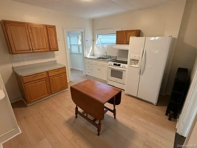 Kitchen featuring wood-finish flooring, white appliances, and light wood cabinetry Kitchen featuring wood-finish flooring, white appliances, and light wood cabinetry