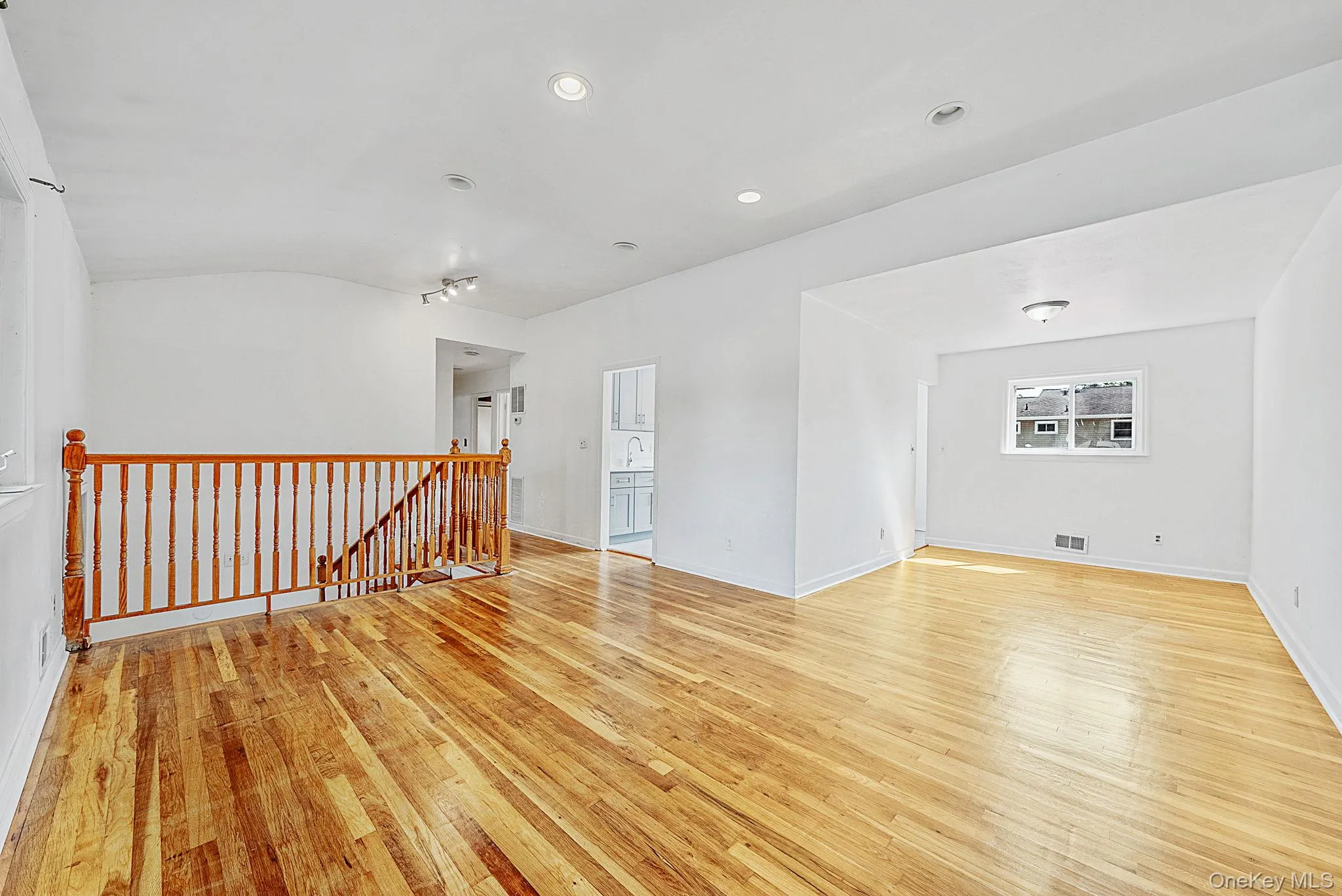 Spacious interior with wood-finish flooring, white walls, and recessed lighting Spacious interior with wood-finish flooring, white walls, and recessed lighting