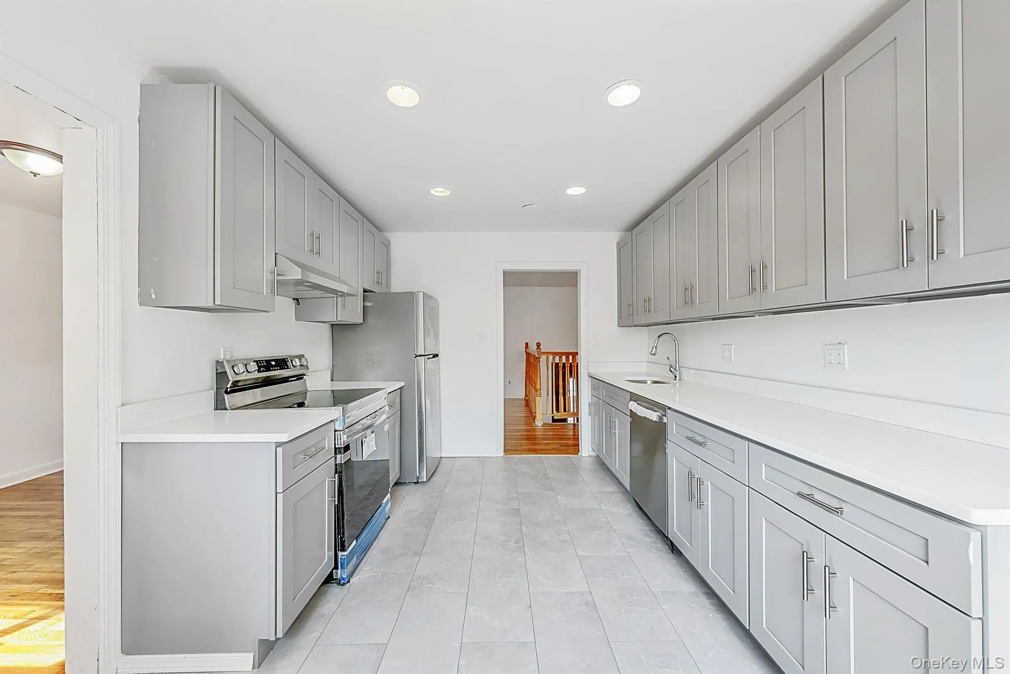 Galley kitchen featuring light gray shaker cabinetry, white countertops, stainless steel appliances, recessed lighting, and tile flooring Galley kitchen featuring light gray shaker cabinetry, white countertops, stainless steel appliances, recessed lighting, and tile flooring