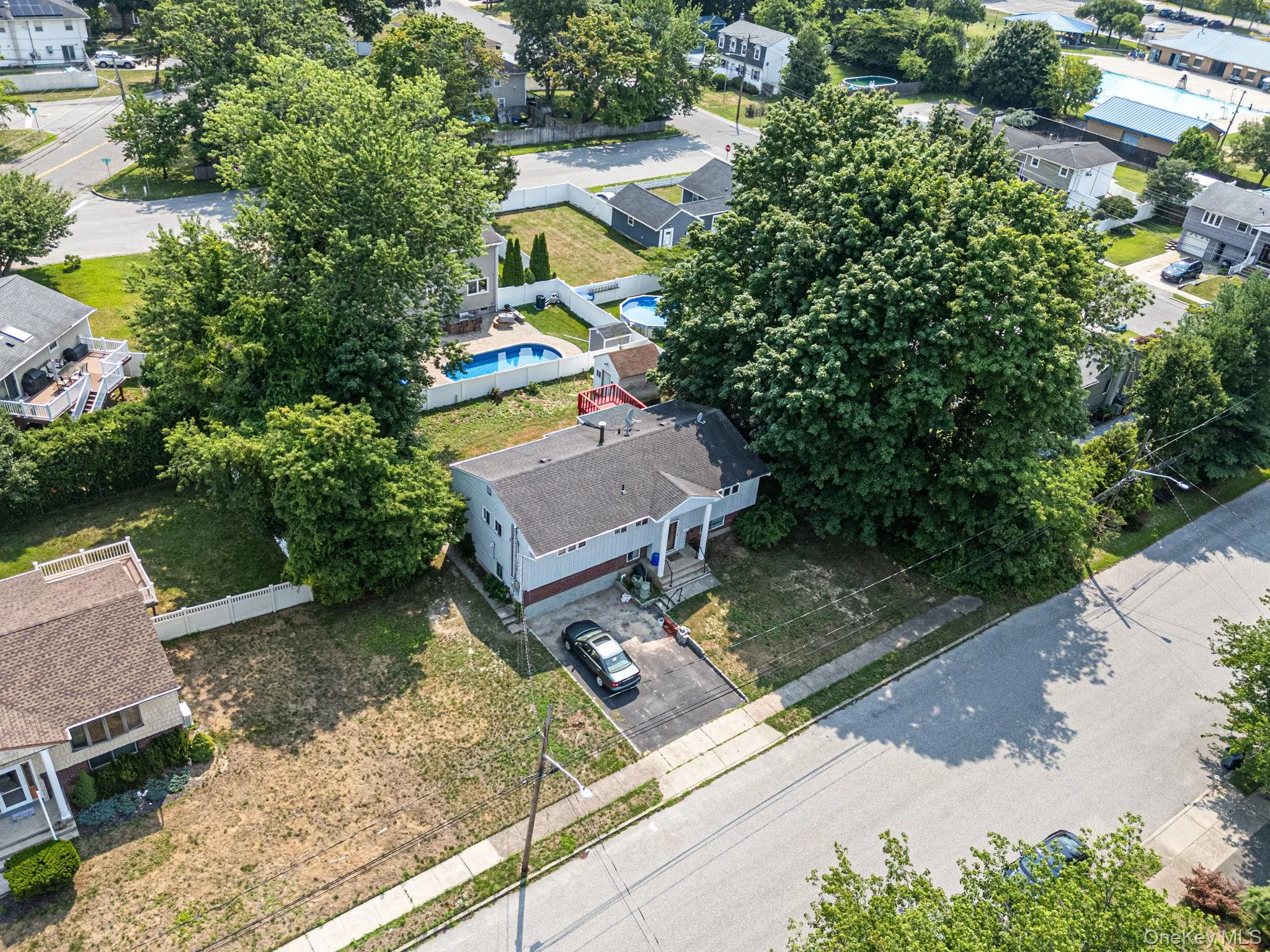 Single-story residence featuring a paved driveway, mature trees, and an in-ground swimming pool Single-story residence featuring a paved driveway, mature trees, and an in-ground swimming pool