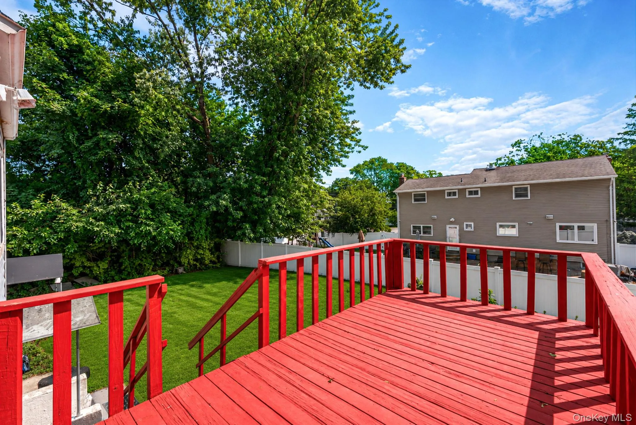 Spacious red-stained wood deck overlooking a fenced backyard with a manicured lawn and mature trees Spacious red-stained wood deck overlooking a fenced backyard with a manicured lawn and mature trees