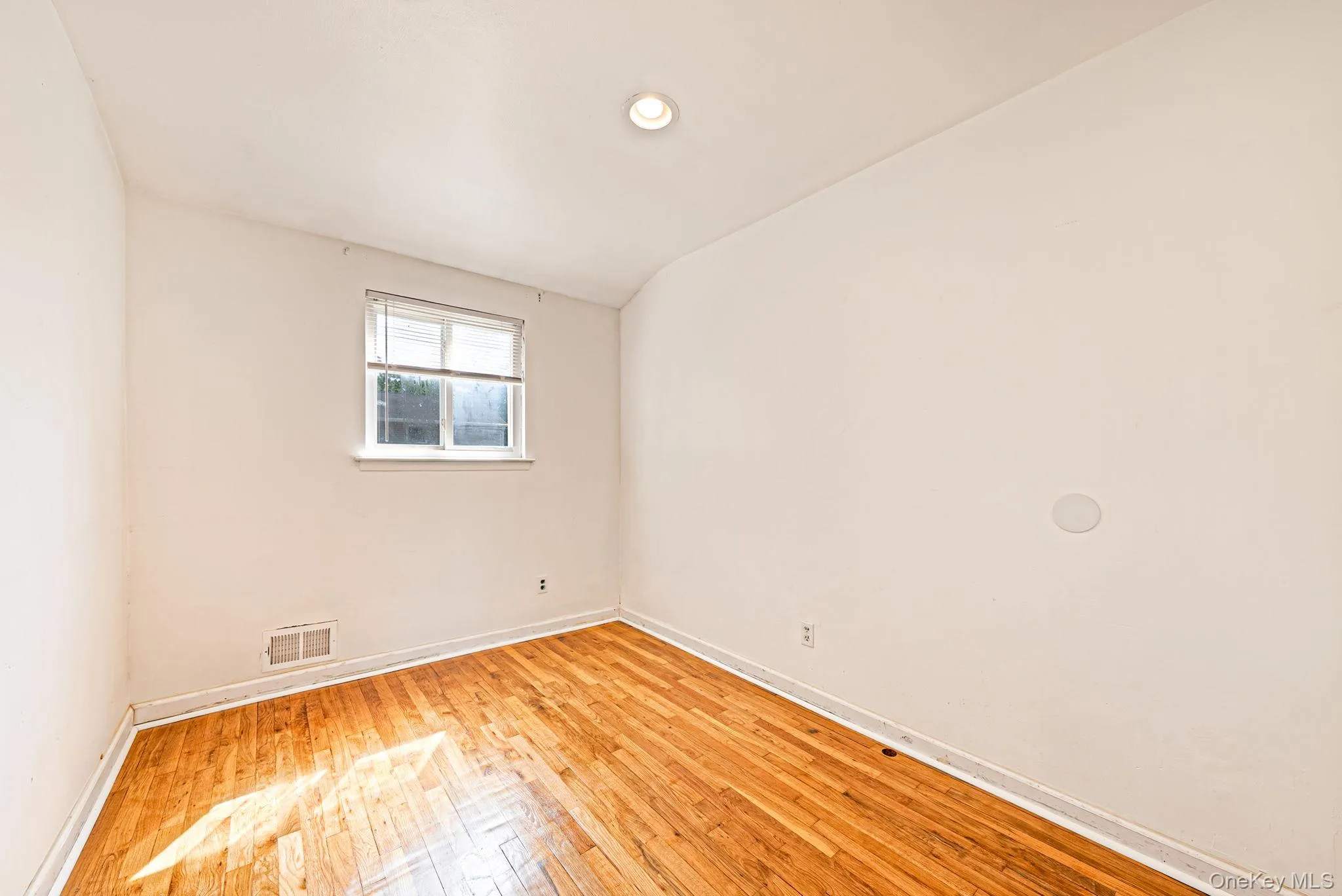 Room featuring wood-finish flooring, white baseboards, a window with blinds, and a ceiling-mounted recessed light Room featuring wood-finish flooring, white baseboards, a window with blinds, and a ceiling-mounted recessed light