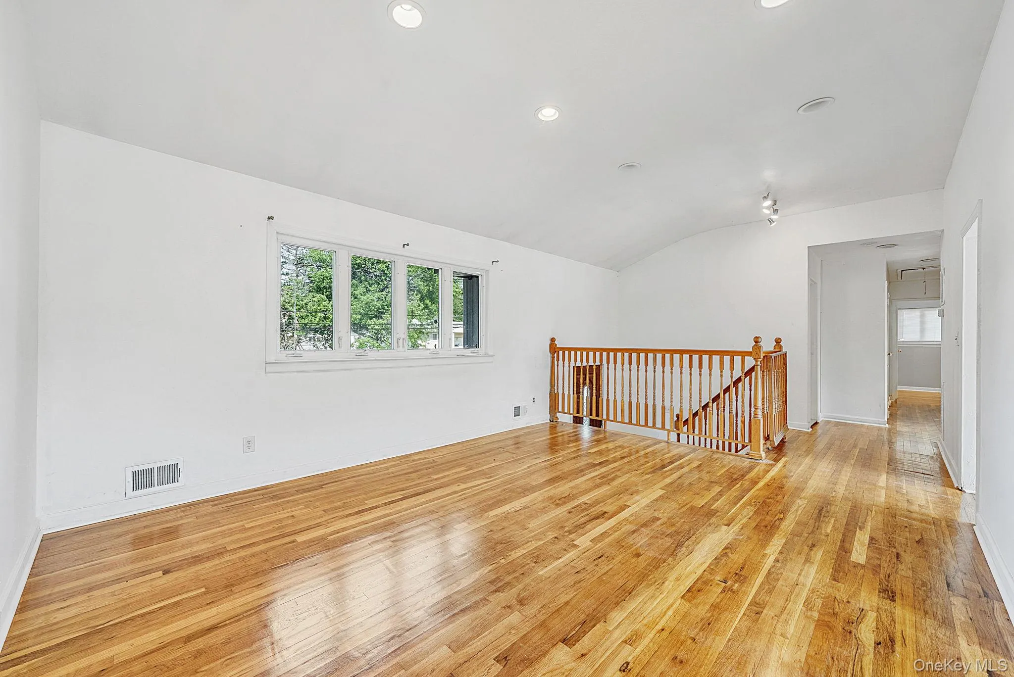 Open concept living area featuring wood-finish flooring, a vaulted ceiling, recessed lighting, and a multi-pane window Open concept living area featuring wood-finish flooring, a vaulted ceiling, recessed lighting, and a multi-pane window