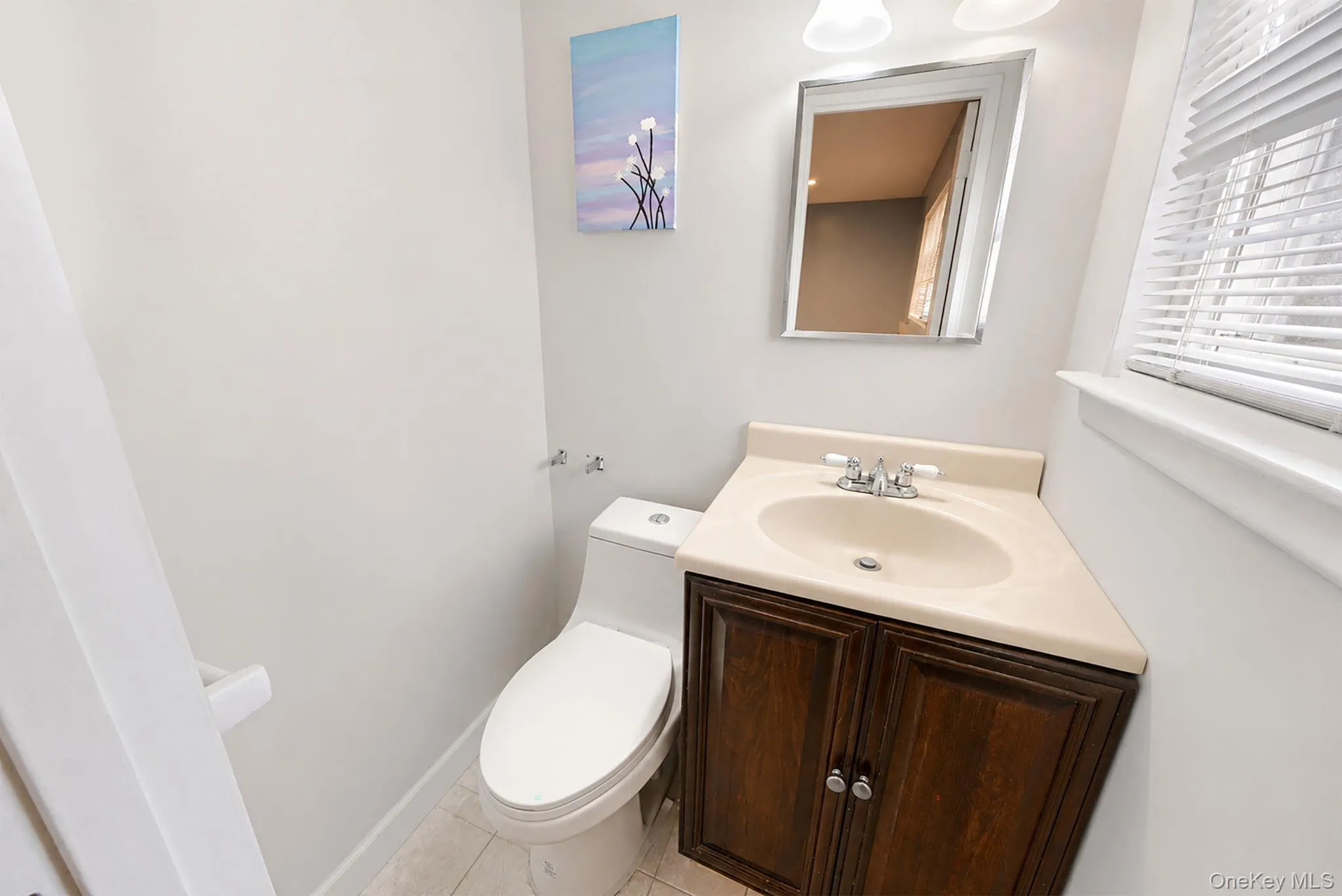 Powder room featuring a single-sink vanity with a wood-finish cabinet and light-toned countertop, a rectangular mirror, and a white toilet Powder room featuring a single-sink vanity with a wood-finish cabinet and light-toned countertop, a rectangular mirror, and a white toilet