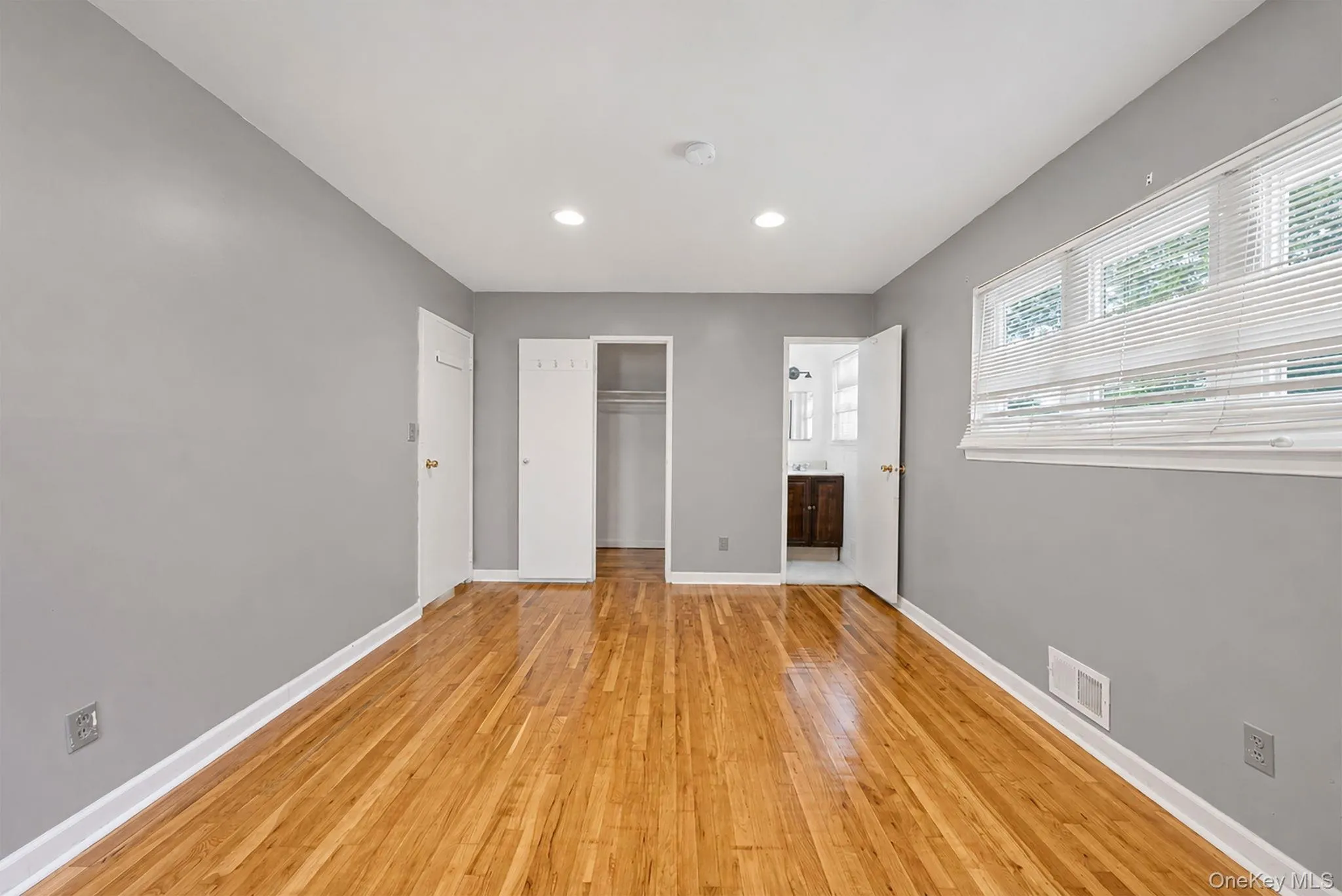 Spacious room featuring wood-finish flooring, recessed lighting, and a large window with horizontal blinds Spacious room featuring wood-finish flooring, recessed lighting, and a large window with horizontal blinds