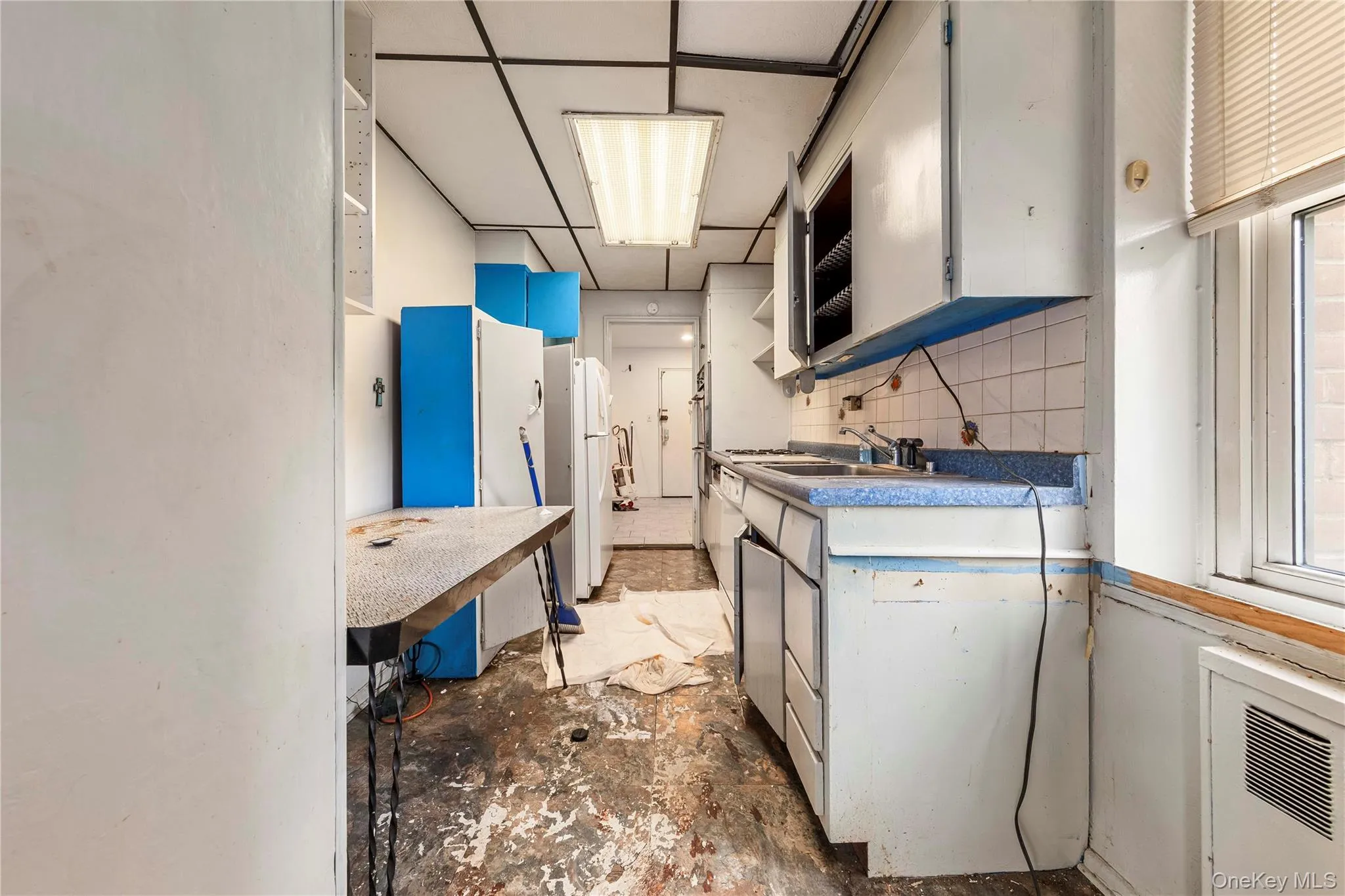 Galley-style kitchen featuring upper and lower cabinetry, a double basin sink, and window with horizontal blinds Galley-style kitchen featuring upper and lower cabinetry, a double basin sink, and window with horizontal blinds