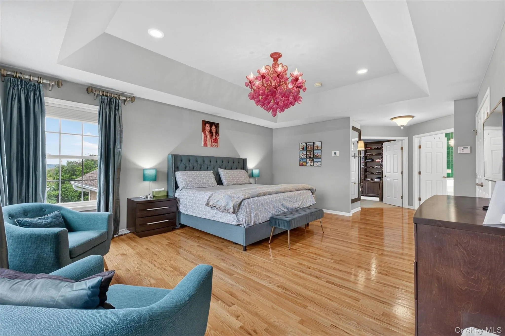 Expansive primary suite with tray ceiling, hardwood floors, sitting area, and scenic views. Expansive primary suite with tray ceiling, hardwood floors, sitting area, and scenic views.