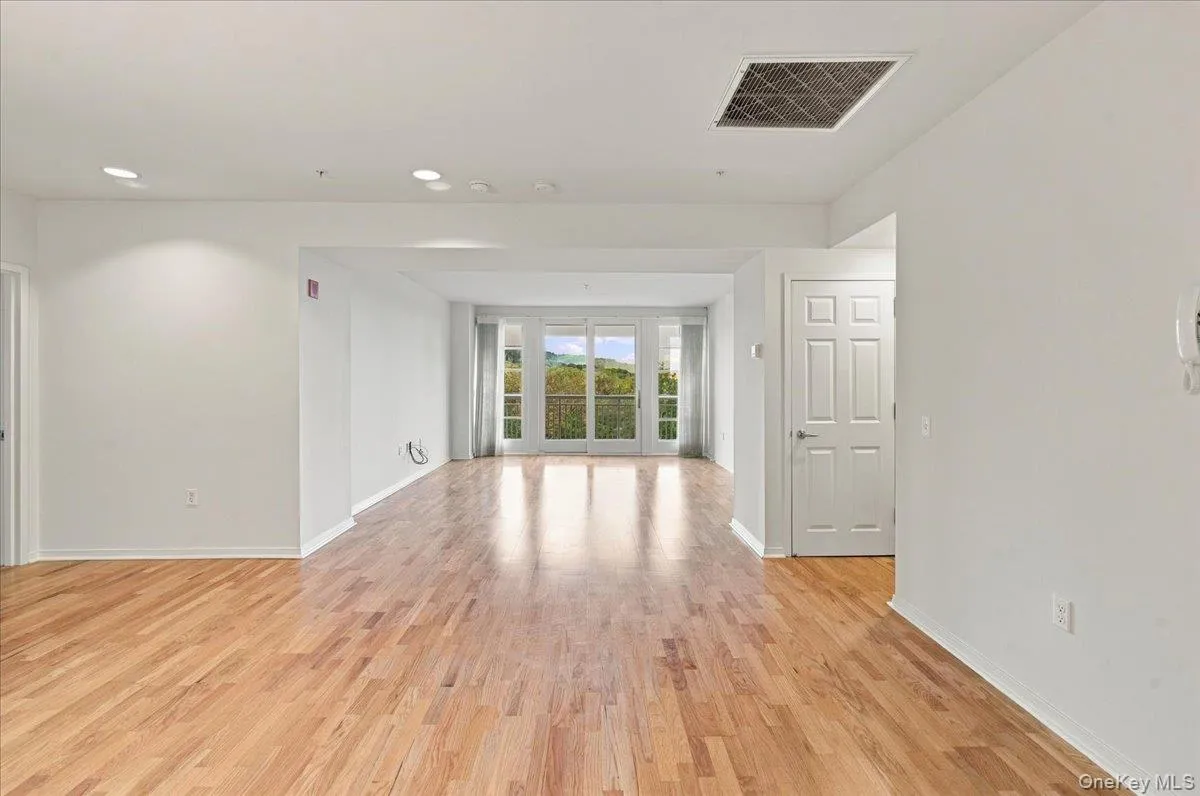 Wood-finish flooring throughout, recessed ceiling lighting, light-colored walls, and a large sliding glass door opening to an exterior balcony Wood-finish flooring throughout, recessed ceiling lighting, light-colored walls, and a large sliding glass door opening to an exterior balcony