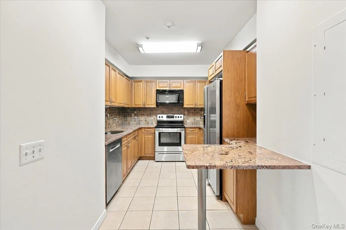 Kitchen featuring wood cabinetry, stainless steel appliances, a tiled backsplash, and a breakfast bar with a stone-finish countertop Kitchen featuring wood cabinetry, stainless steel appliances, a tiled backsplash, and a breakfast bar with a stone-finish countertop