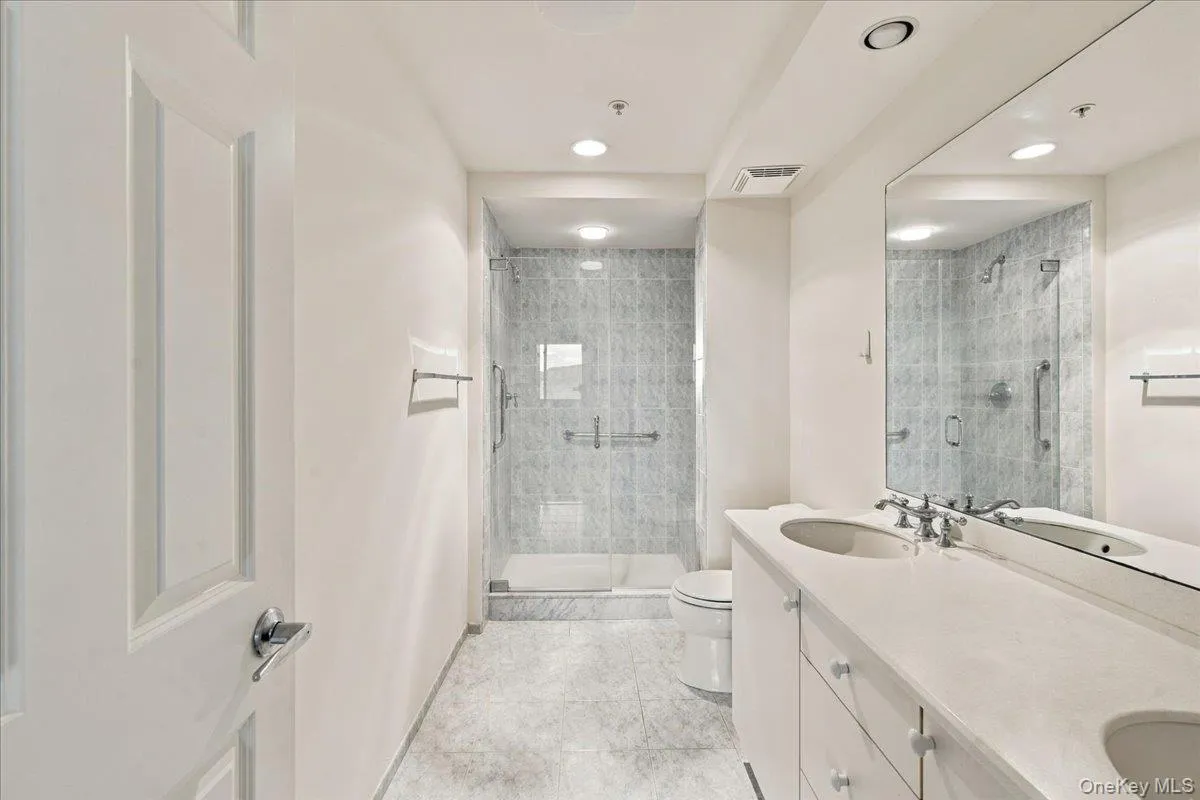 Double vanity with integrated sinks, frameless mirrored wall, glass-enclosed shower, tiled shower walls, and recessed lighting Double vanity with integrated sinks, frameless mirrored wall, glass-enclosed shower, tiled shower walls, and recessed lighting