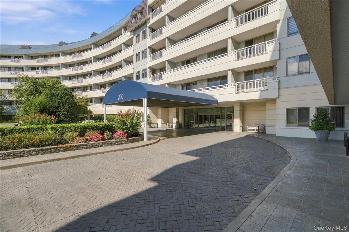 Curved multi-story building exterior with individual balconies, covered entryway with a blue canopy, and a paver driveway Curved multi-story building exterior with individual balconies, covered entryway with a blue canopy, and a paver driveway