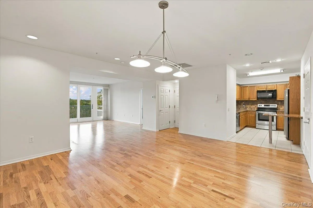 Hardwood flooring throughout the main living area, with a kitchen featuring wood cabinetry, stainless steel appliances, and a tiled floor Hardwood flooring throughout the main living area, with a kitchen featuring wood cabinetry, stainless steel appliances, and a tiled floor