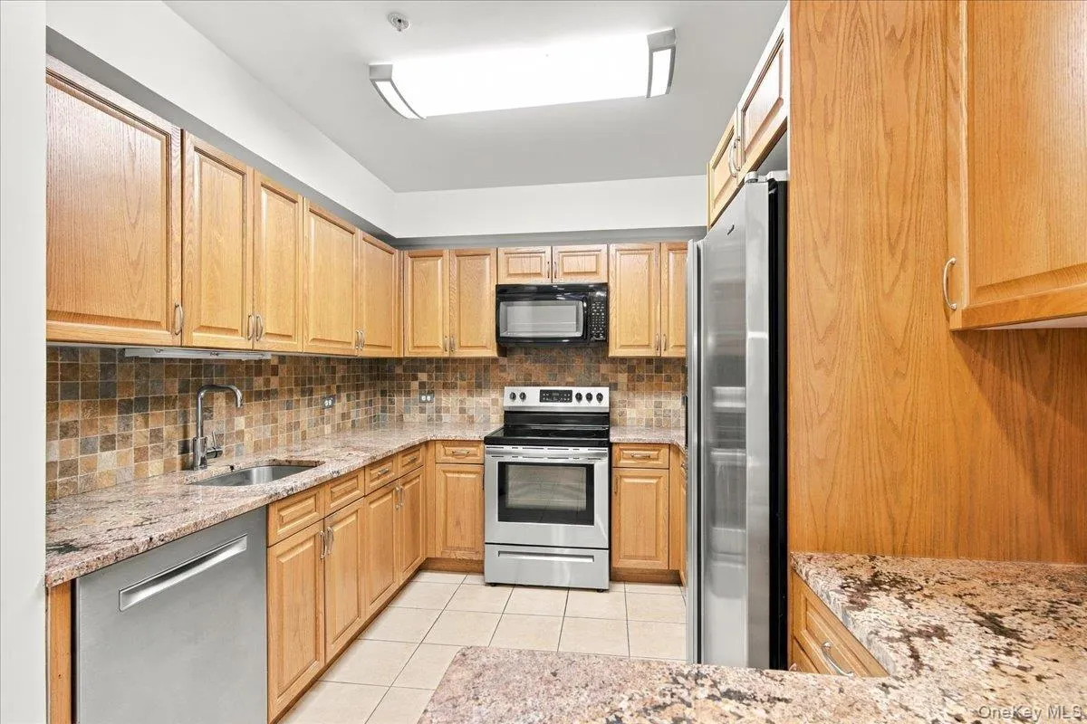 Kitchen featuring wood cabinetry, stainless steel appliances, tiled backsplash, and stone countertops Kitchen featuring wood cabinetry, stainless steel appliances, tiled backsplash, and stone countertops