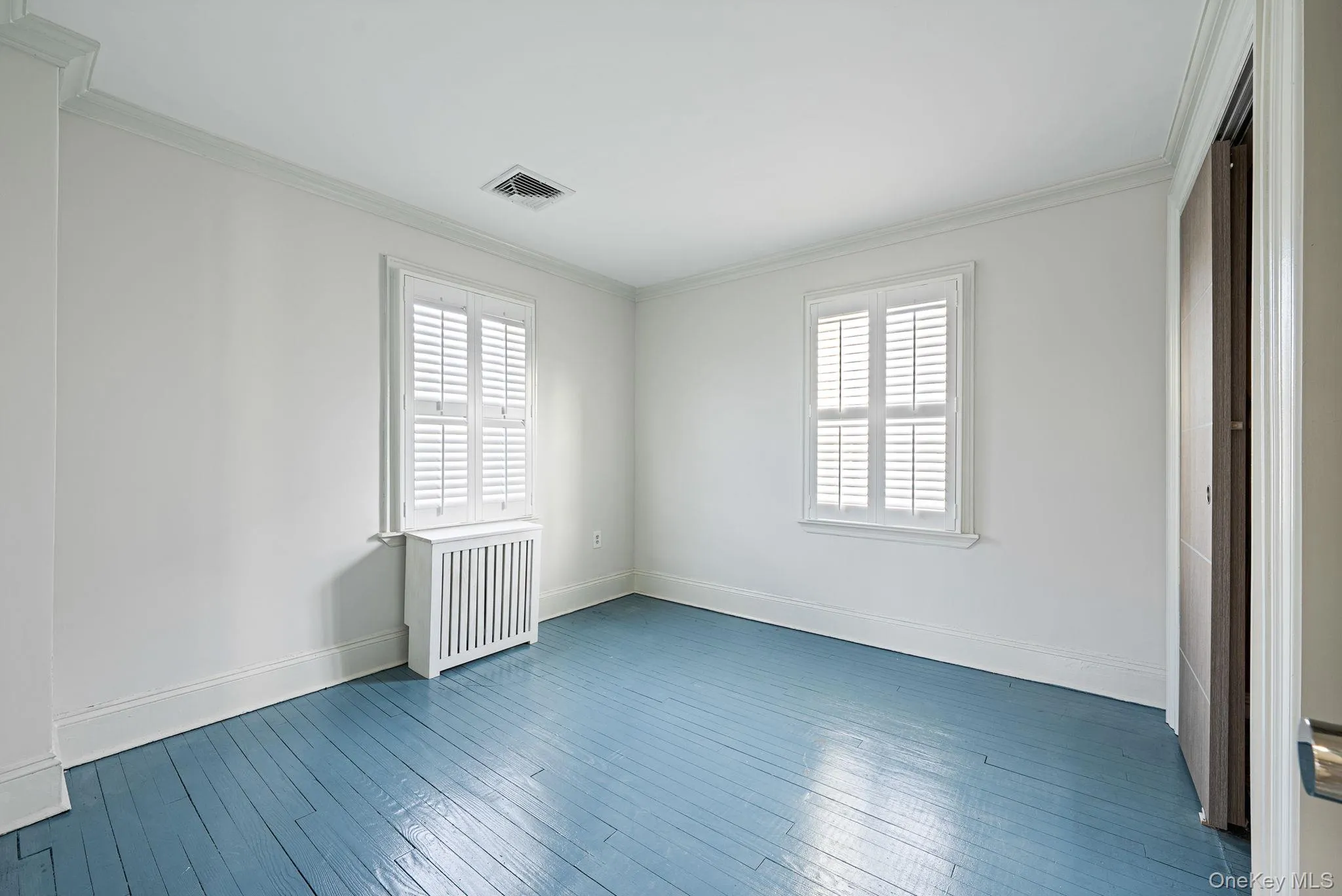 Unfurnished bedroom featuring multiple windows, crown molding, radiator, and dark wood-style flooring Unfurnished bedroom featuring multiple windows, crown molding, radiator, and dark wood-style flooring