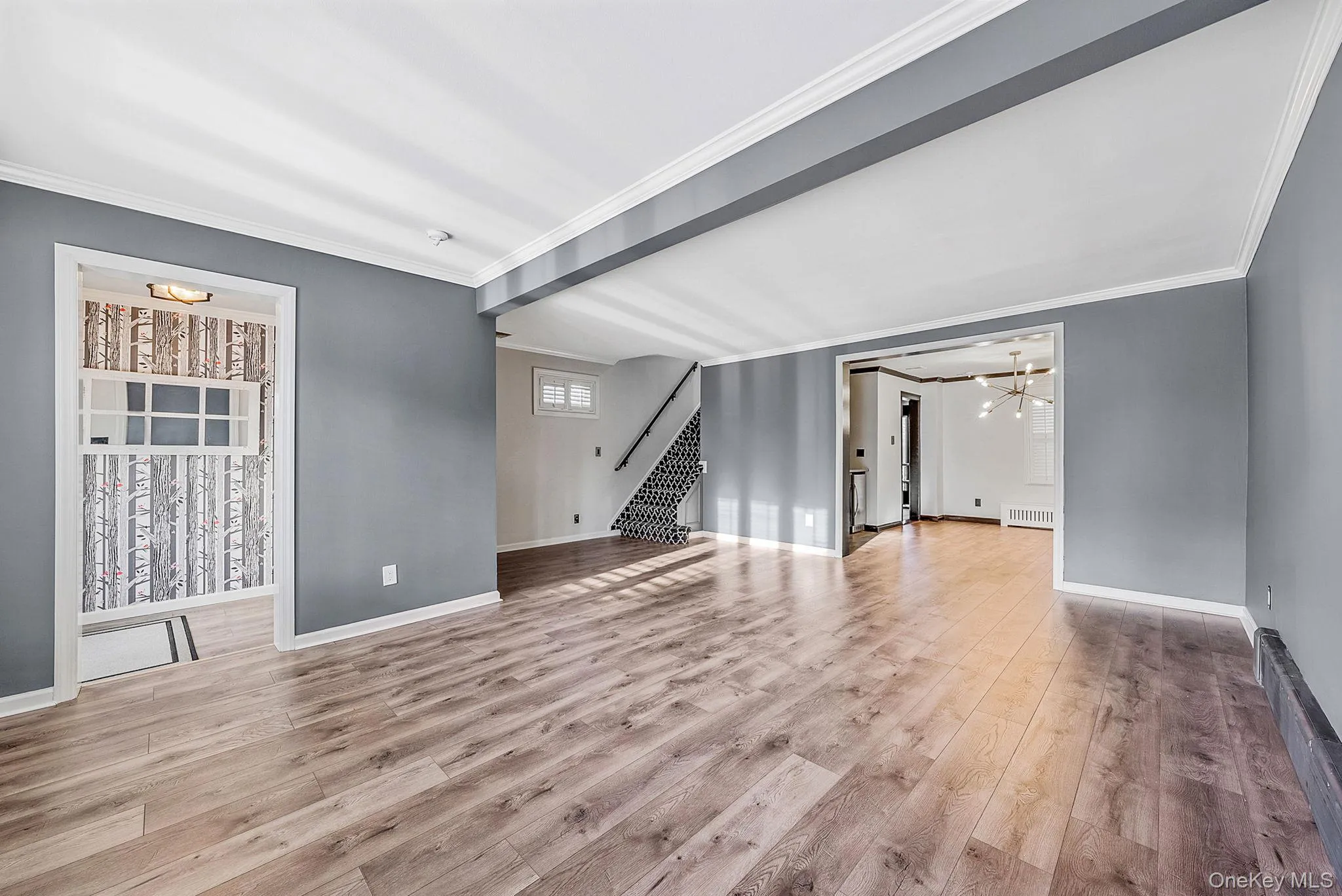 Unfurnished living room with ornamental molding, a chandelier, light wood-style floors, and stairway Unfurnished living room with ornamental molding, a chandelier, light wood-style floors, and stairway