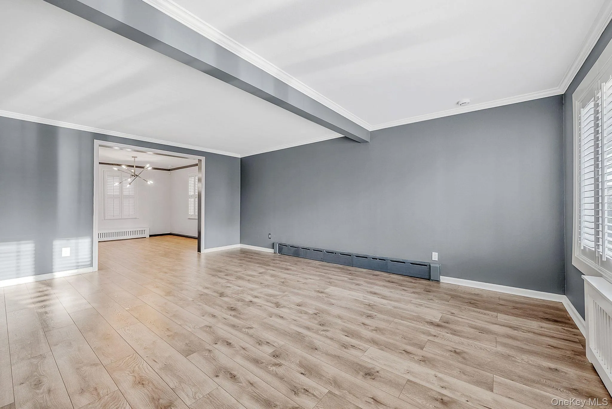 Unfurnished room with crown molding, light wood finished floors, a baseboard radiator, beam ceiling, and radiator Unfurnished room with crown molding, light wood finished floors, a baseboard radiator, beam ceiling, and radiator