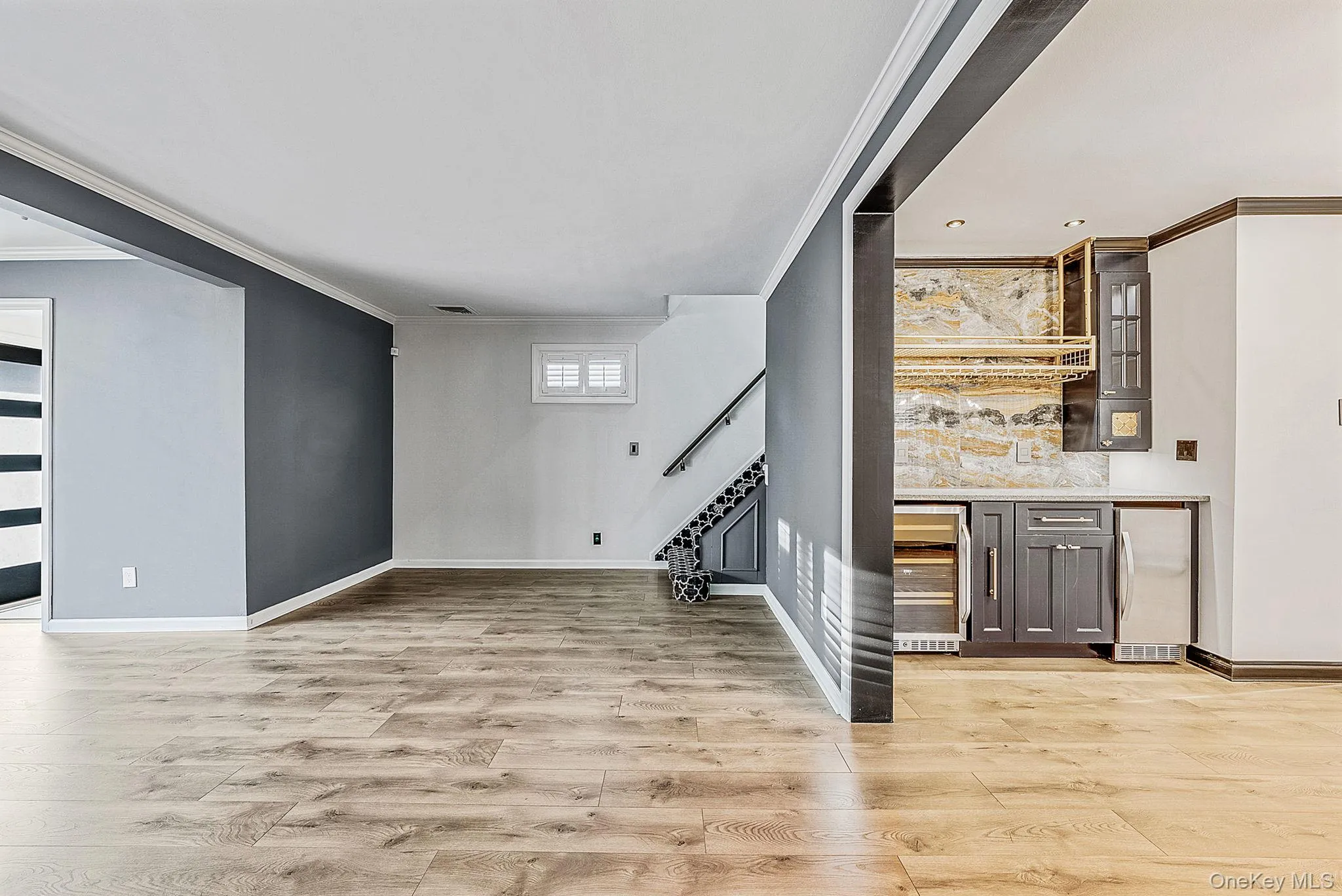 Indoor bar with stainless steel fridge, glass insert cabinets, ornamental molding, light wood-style flooring, and beverage cooler Indoor bar with stainless steel fridge, glass insert cabinets, ornamental molding, light wood-style flooring, and beverage cooler