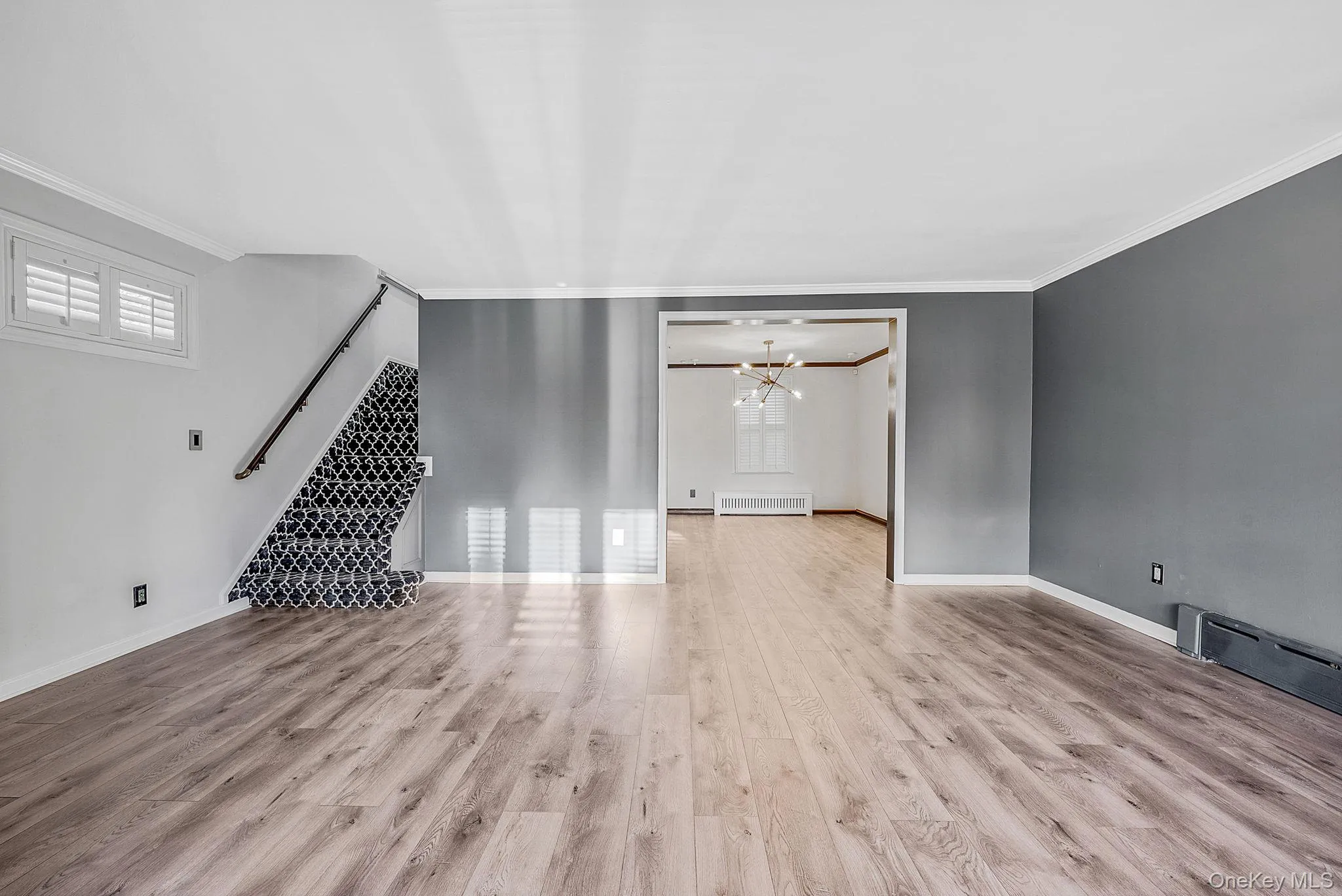 Unfurnished living room featuring a chandelier, light wood finished floors, crown molding, radiator heating unit, and a baseboard radiator Unfurnished living room featuring a chandelier, light wood finished floors, crown molding, radiator heating unit, and a baseboard radiator