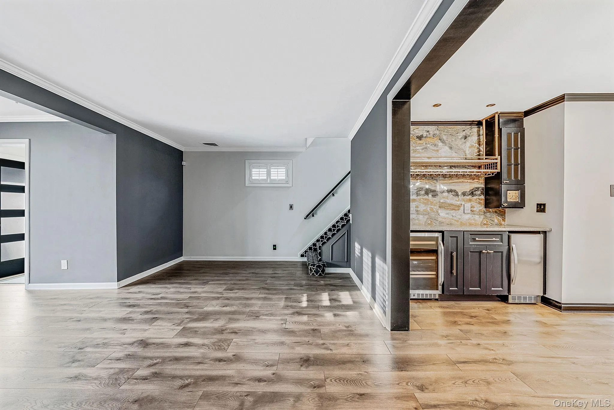 Indoor wet bar with stainless steel refrigerator, crown molding, beverage cooler, stairs, and light stone countertops Indoor wet bar with stainless steel refrigerator, crown molding, beverage cooler, stairs, and light stone countertops