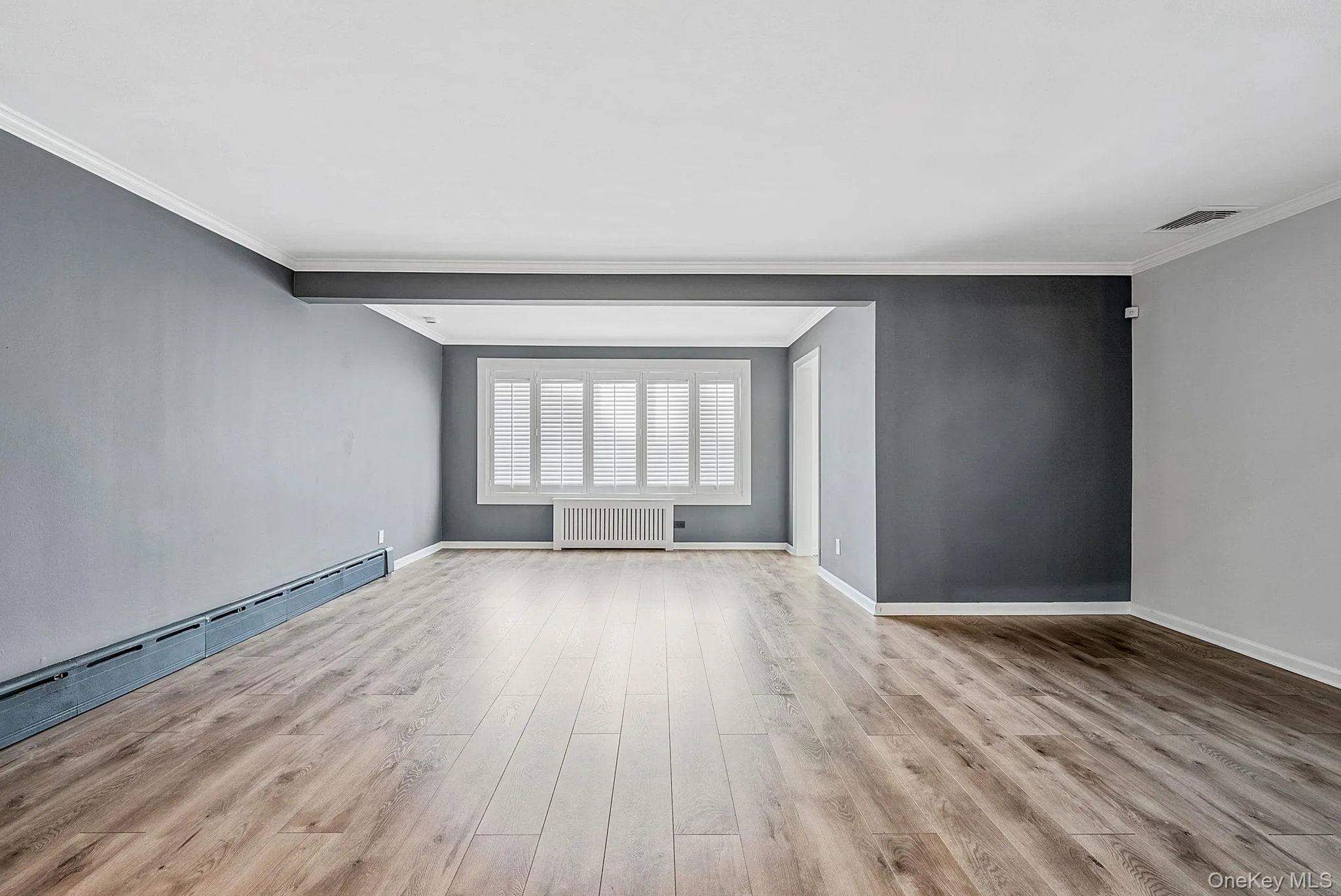 Empty room featuring radiator, light wood-style floors, and ornamental molding Empty room featuring radiator, light wood-style floors, and ornamental molding
