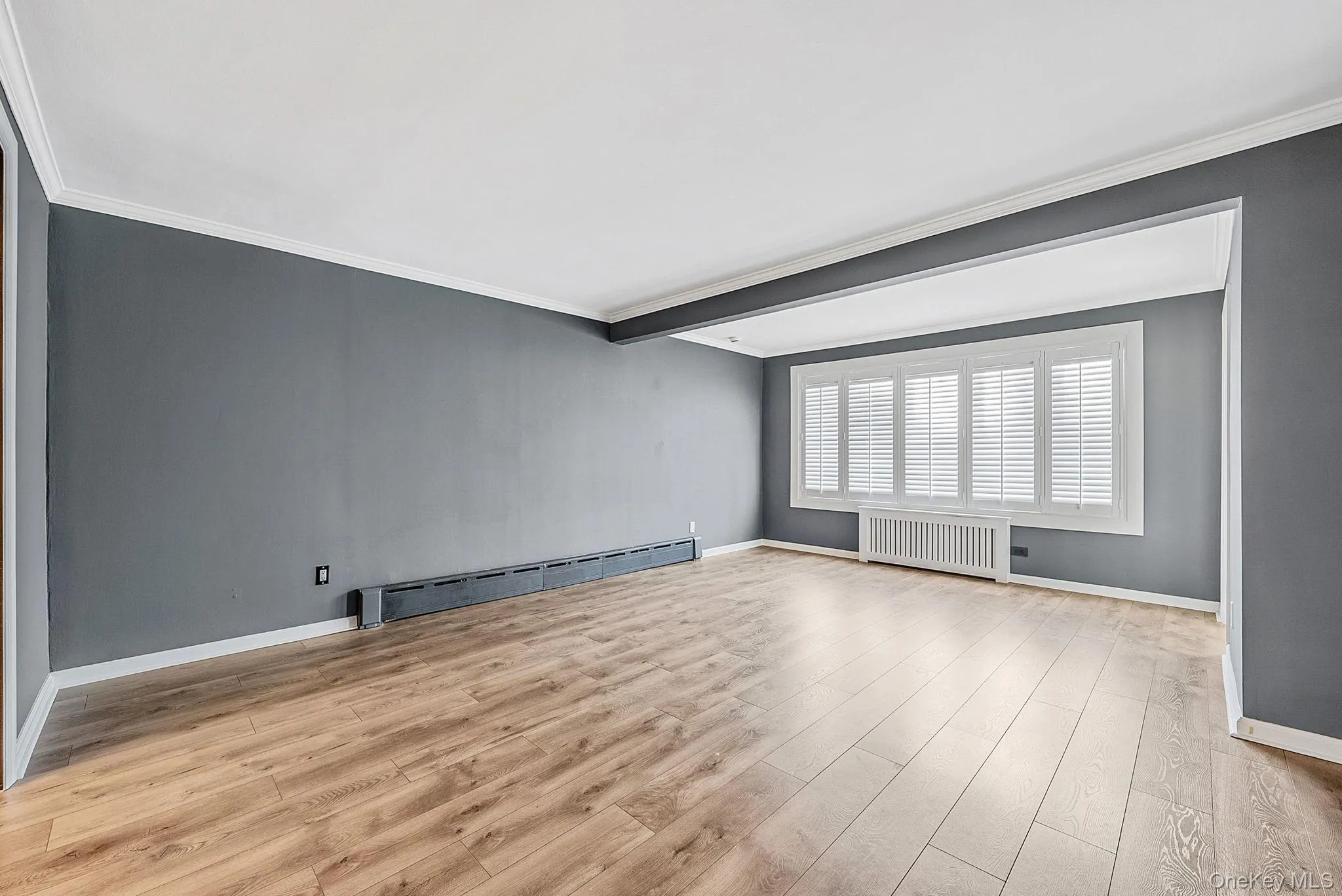 Unfurnished room featuring ornamental molding, baseboard heating, radiator, light wood-style flooring, and beam ceiling Unfurnished room featuring ornamental molding, baseboard heating, radiator, light wood-style flooring, and beam ceiling