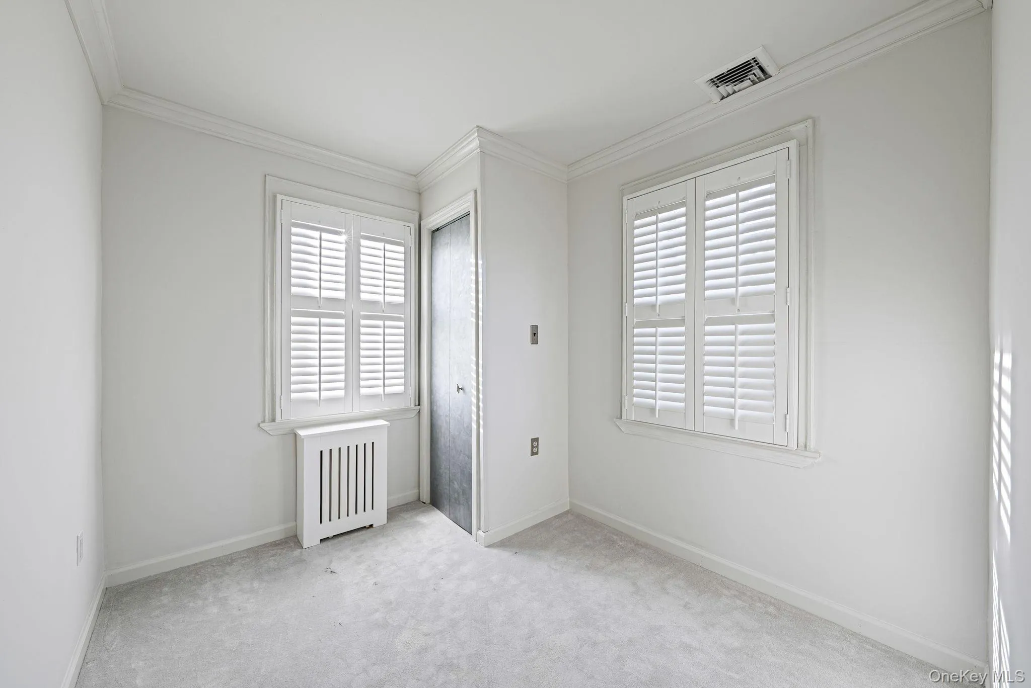 Unfurnished bedroom featuring radiator heating unit, crown molding, multiple windows, and carpet Unfurnished bedroom featuring radiator heating unit, crown molding, multiple windows, and carpet