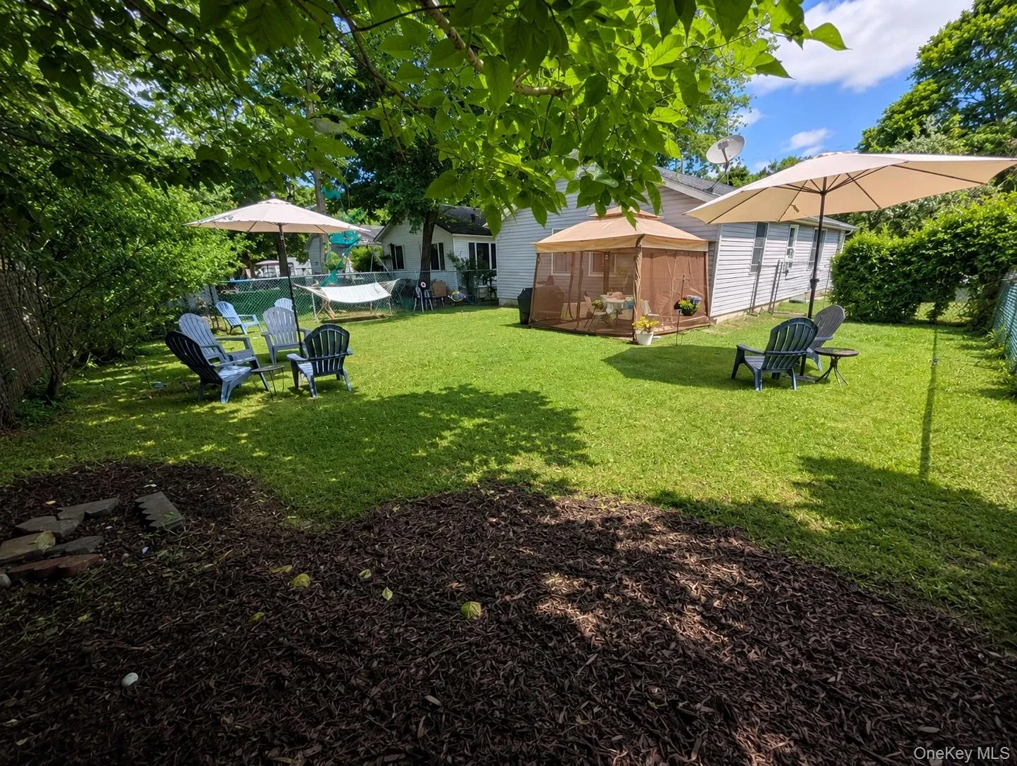 Expansive backyard featuring a lush lawn, mature trees, a screened gazebo, and a chain-link fence Expansive backyard featuring a lush lawn, mature trees, a screened gazebo, and a chain-link fence