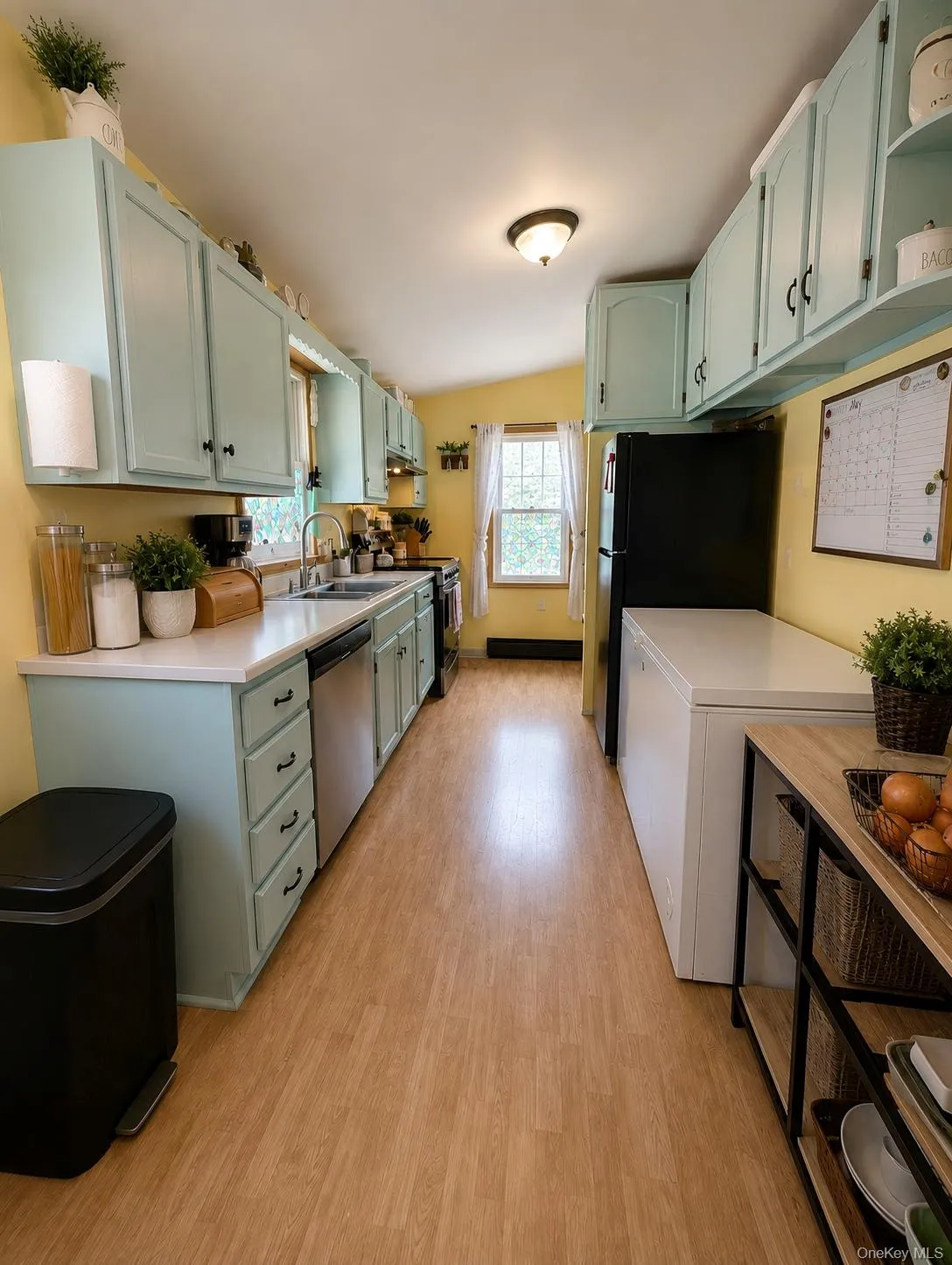 Galley kitchen featuring light wood-finish flooring, light-toned cabinetry, stainless steel range with overhead ventilation, and a stainless steel sink Galley kitchen featuring light wood-finish flooring, light-toned cabinetry, stainless steel range with overhead ventilation, and a stainless steel sink