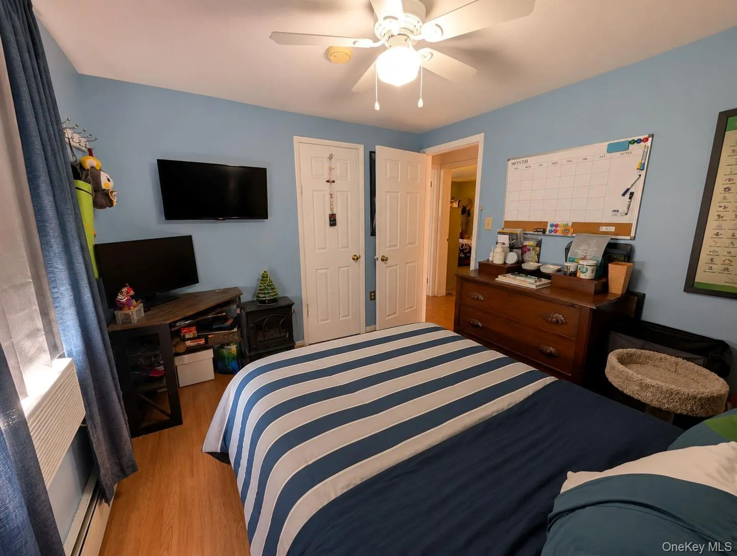 Bedroom featuring wood-finish flooring, a ceiling fan with integrated lighting, and light blue wall tones Bedroom featuring wood-finish flooring, a ceiling fan with integrated lighting, and light blue wall tones