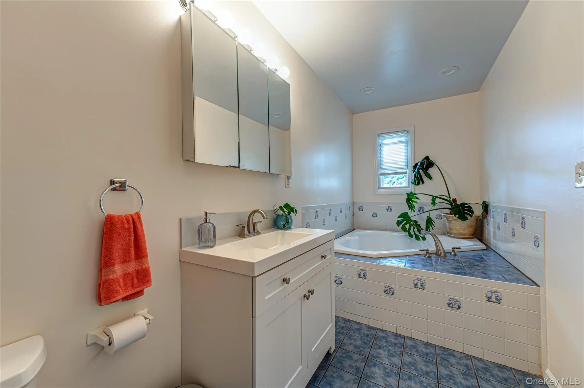 Bathroom featuring a built-in corner soaking tub with blue tile surround, white vanity with integrated sink, chrome faucet, and mirrored medicine cabinet Bathroom featuring a built-in corner soaking tub with blue tile surround, white vanity with integrated sink, chrome faucet, and mirrored medicine cabinet