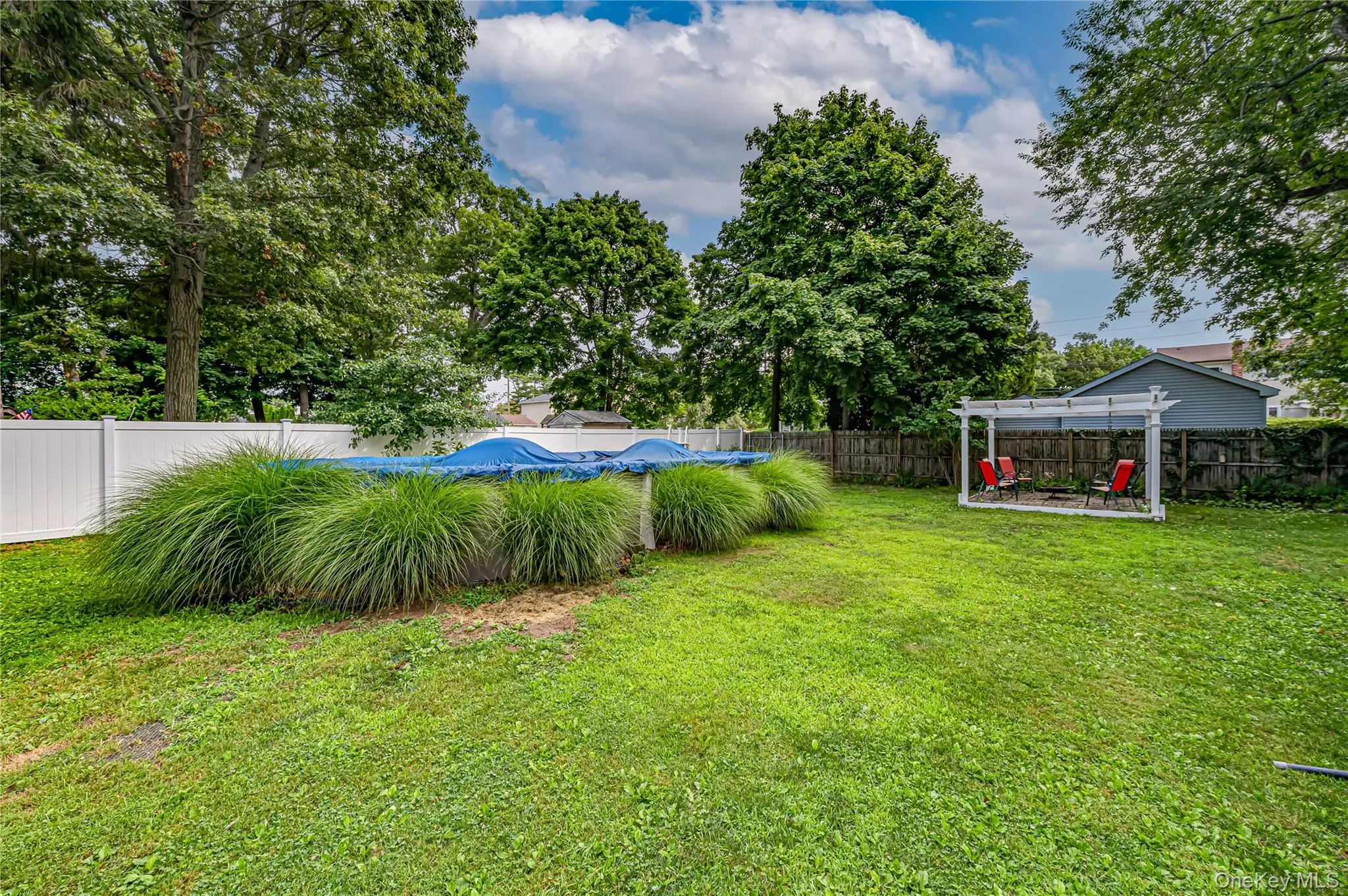 Expansive backyard featuring a covered above-ground pool that sellers are fighting to buyers, a white pergola, and mature trees providing natural shading Expansive backyard featuring a covered above-ground pool that sellers are fighting to buyers, a white pergola, and mature trees providing natural shading