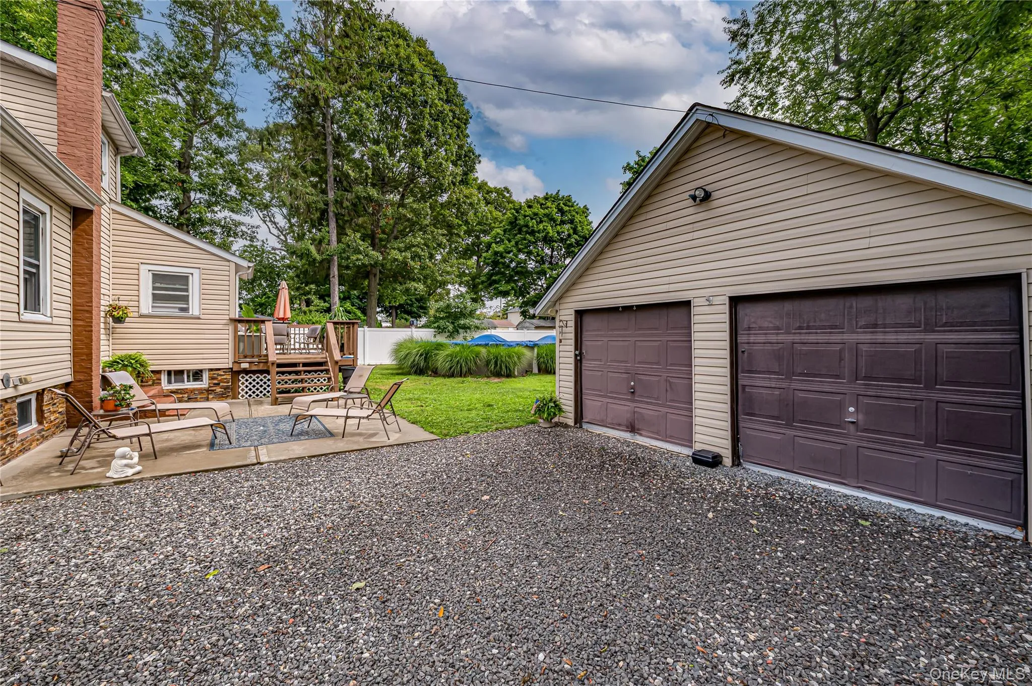 Two-car detached garage with panel doors, gravel driveway, concrete patio, and a tiered wood deck with railing Two-car detached garage with panel doors, gravel driveway, concrete patio, and a tiered wood deck with railing